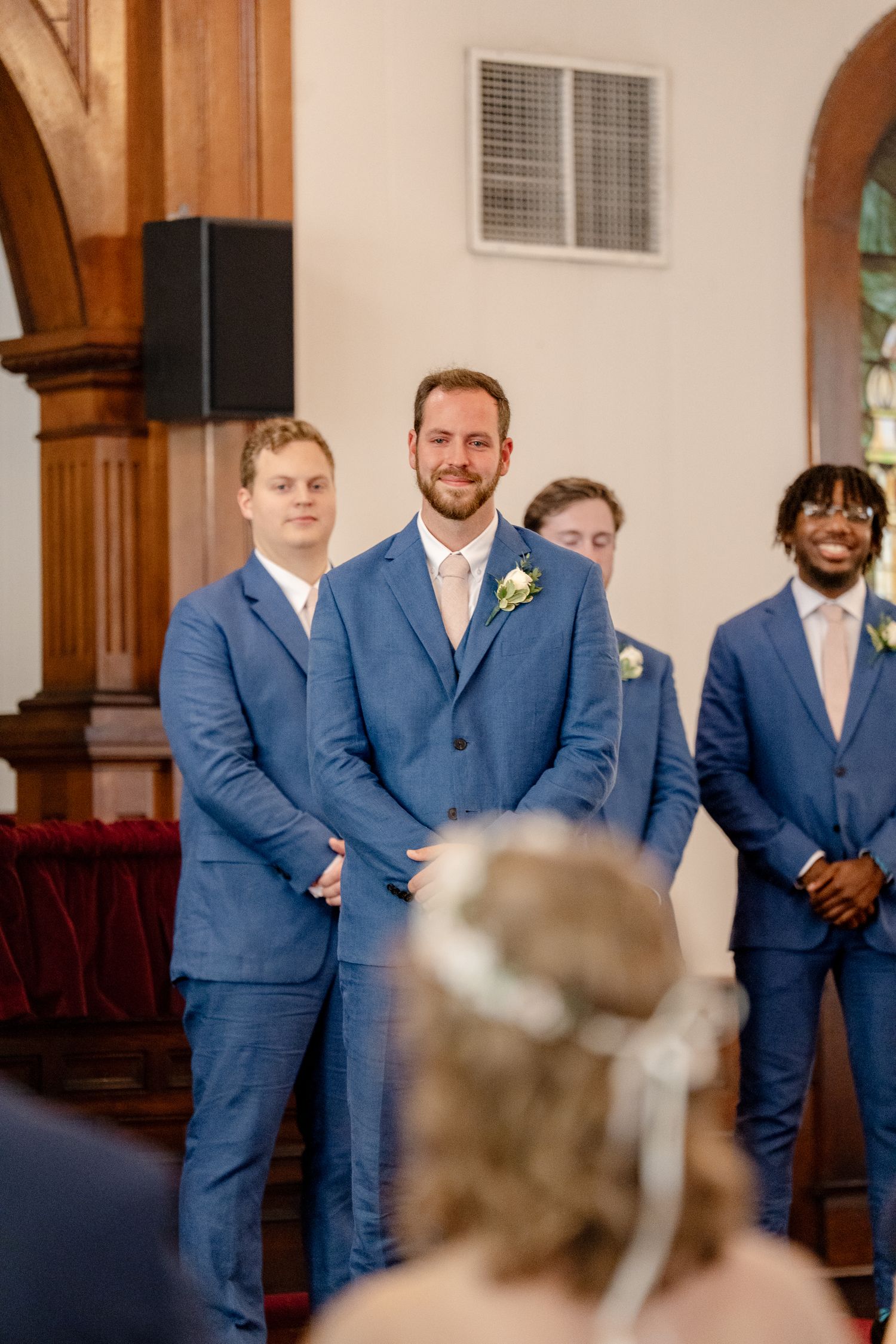 Groomsmen in matching blue suits stand at attention during church wedding ceremony.