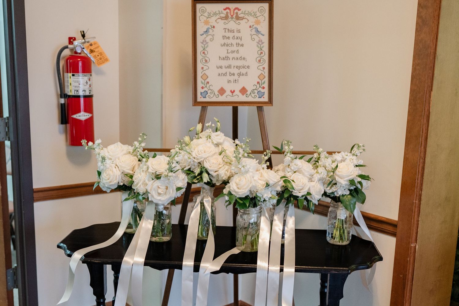 White floral arrangements and candles decorate a rustic indoor venue with wooden beams and framed artwork on the walls.