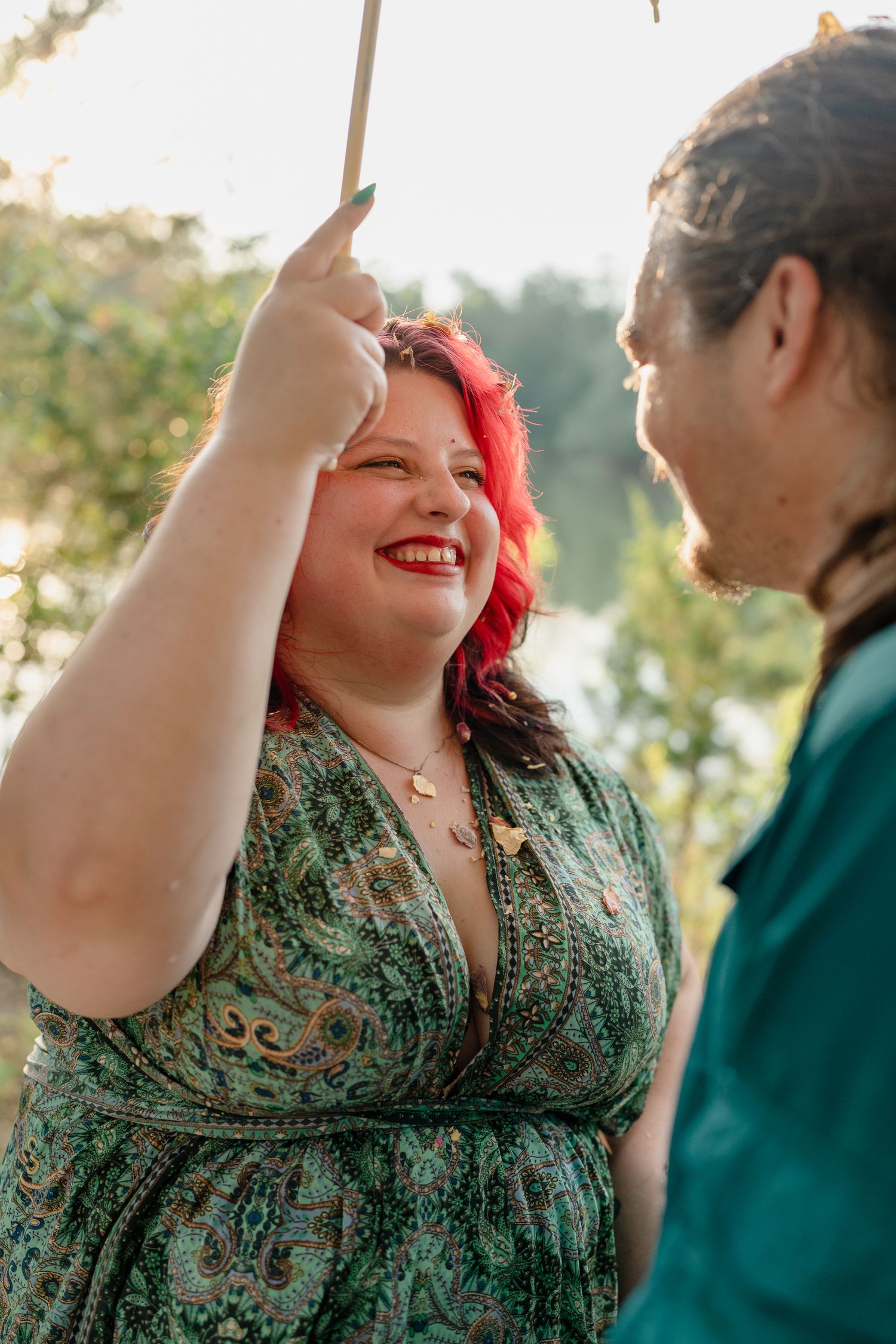 A couple laughs together outdoors in golden sunlight, with one wearing a green patterned dress.