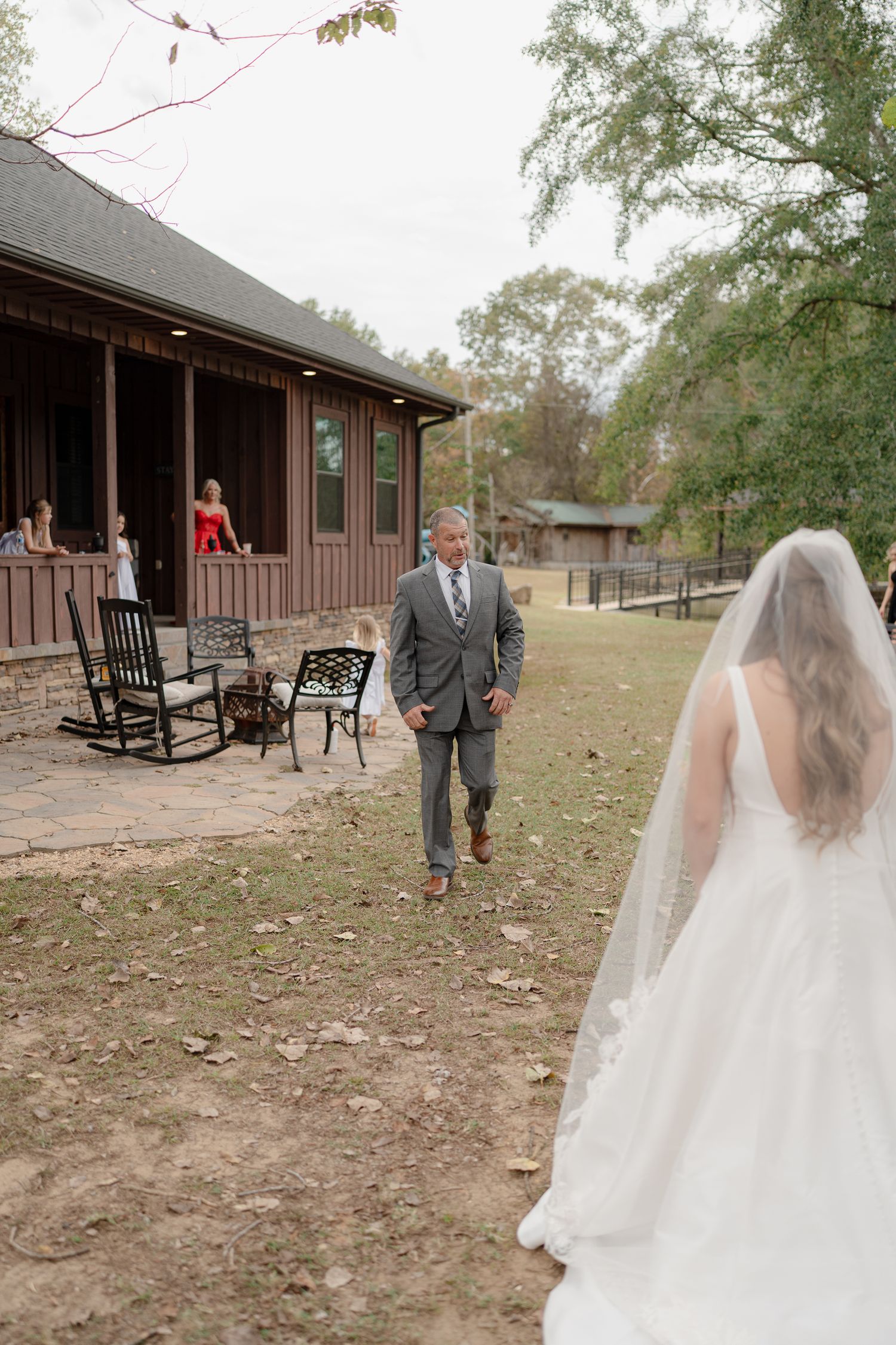 First look wedding photos at a rustic outdoor venue with wooden buildings and rocking chairs on a porch.