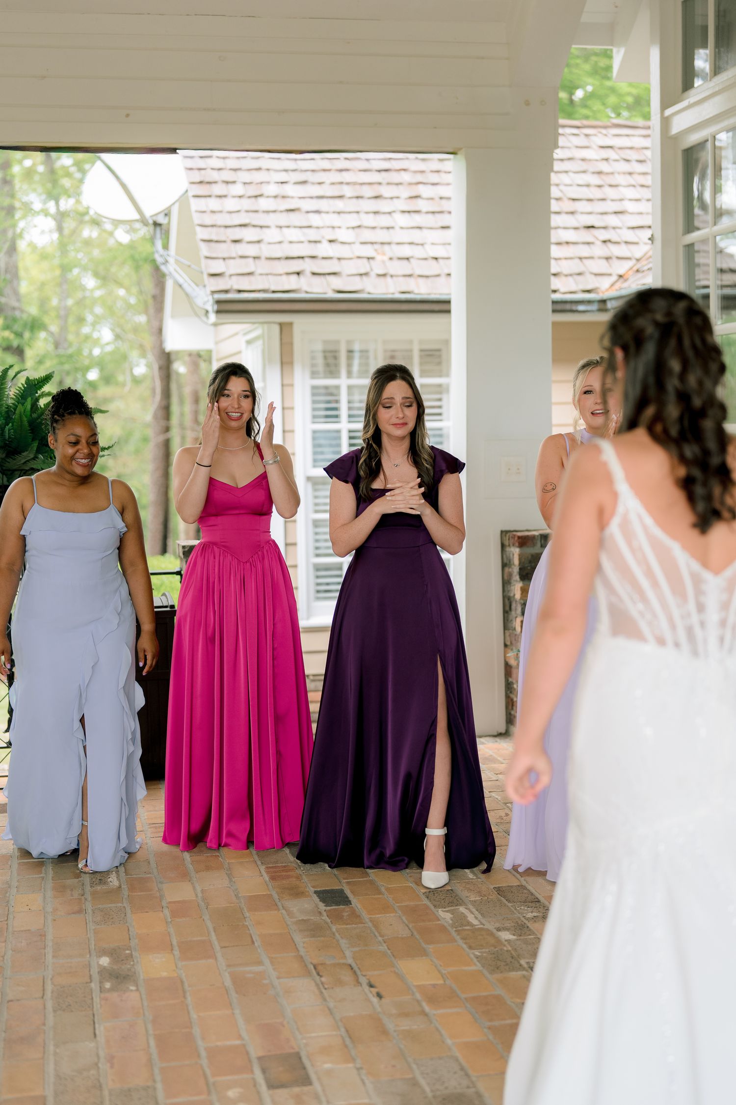 Bridesmaids in colorful gowns react with joy as bride reveals her wedding dress during a bridal party first look.