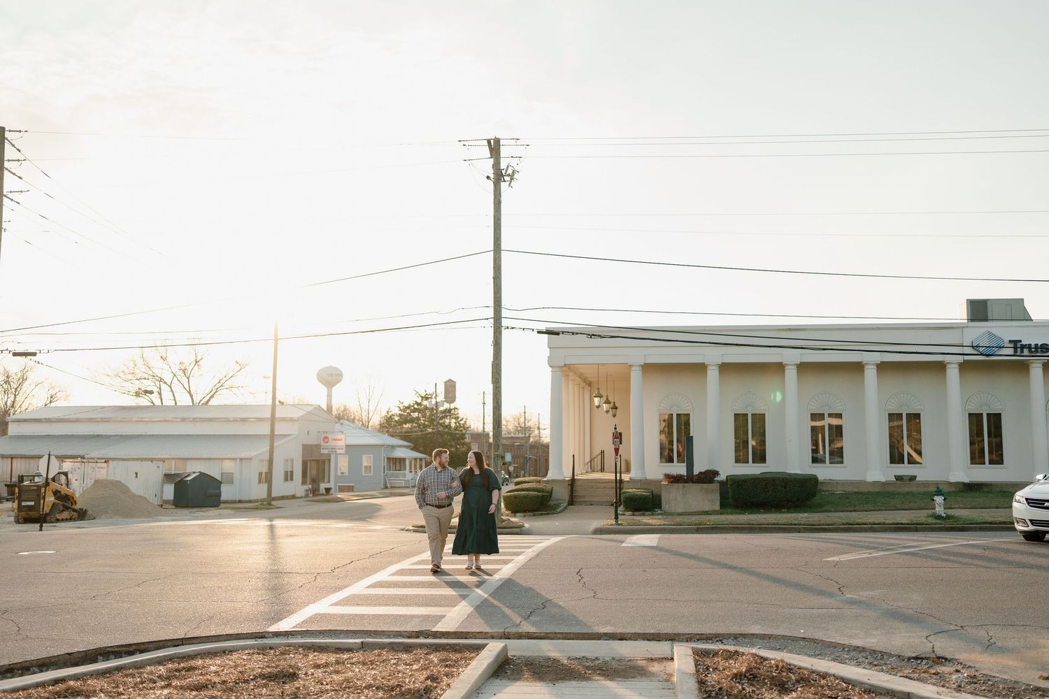 Couple walking across a sunny street toward a white columned building in a small town setting.