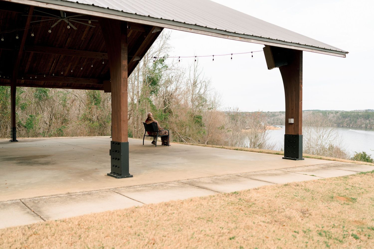 Person sitting alone under a large open pavilion overlooking a serene river landscape.
