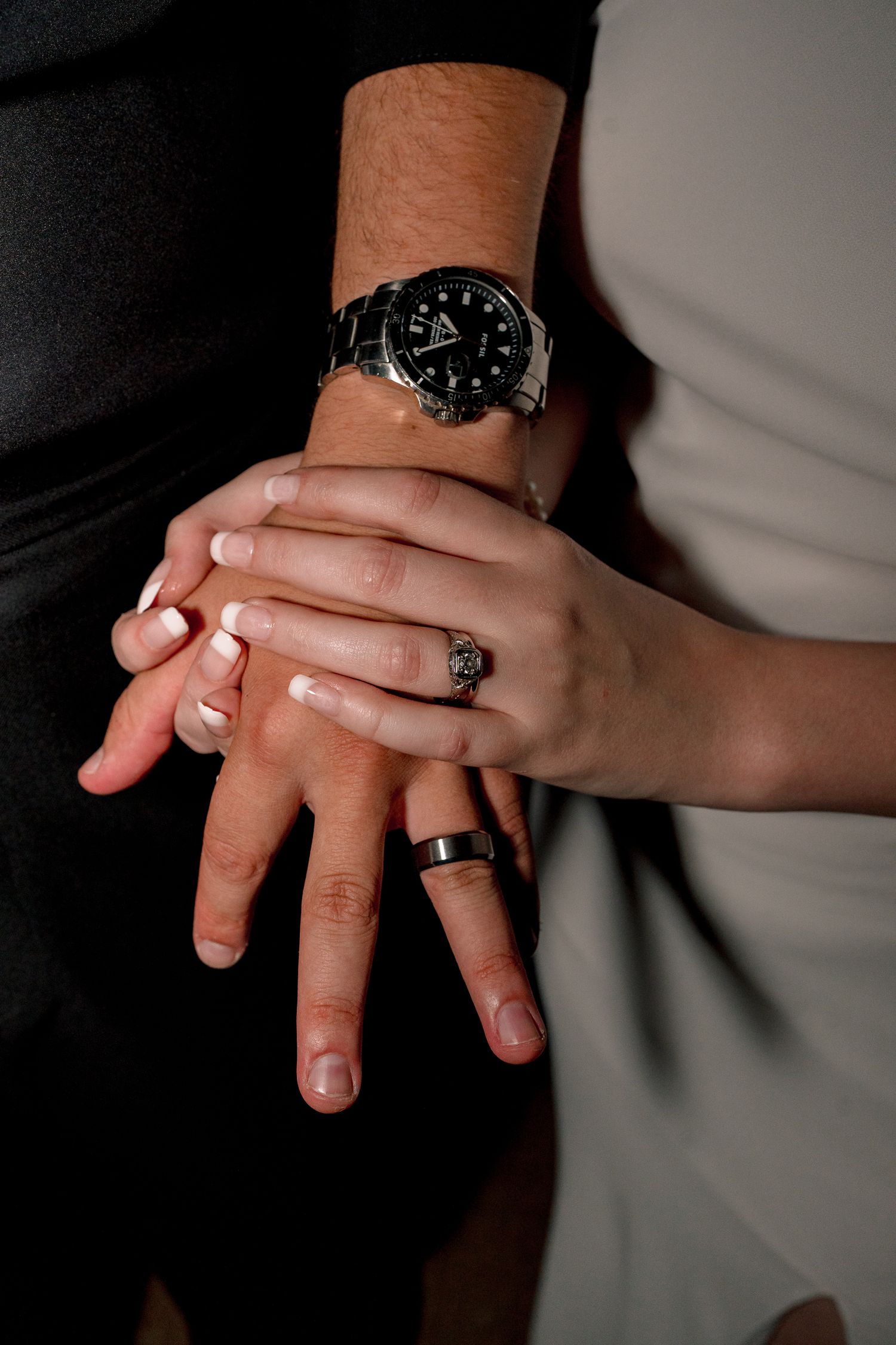 Close-up of wedding couple hands showing rings, with groom wearing a black watch and bride displaying elegant French manicure.