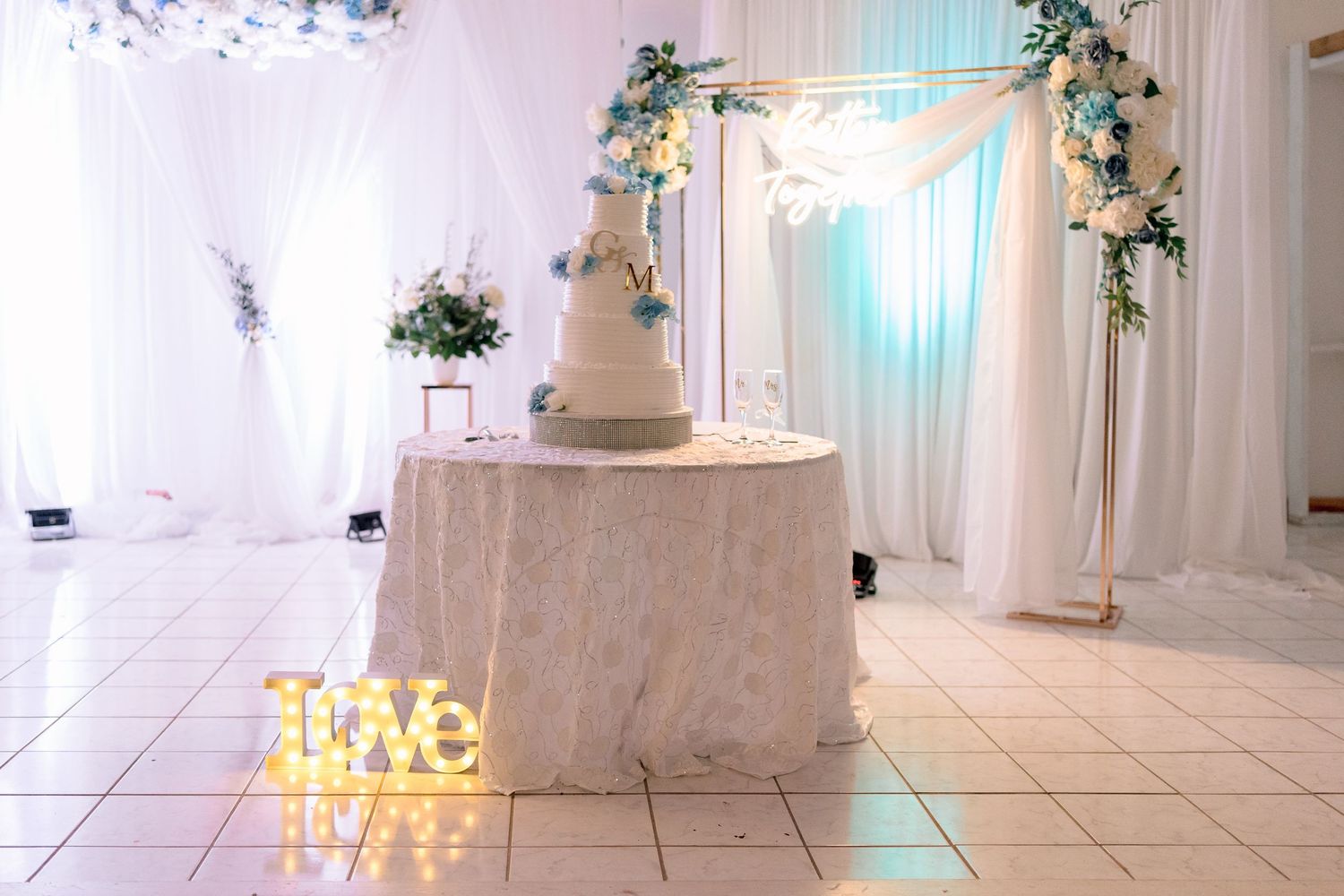 Elegant white wedding venue interior with draped fabric, floral arrangements and uplighting creating a romantic atmosphere.