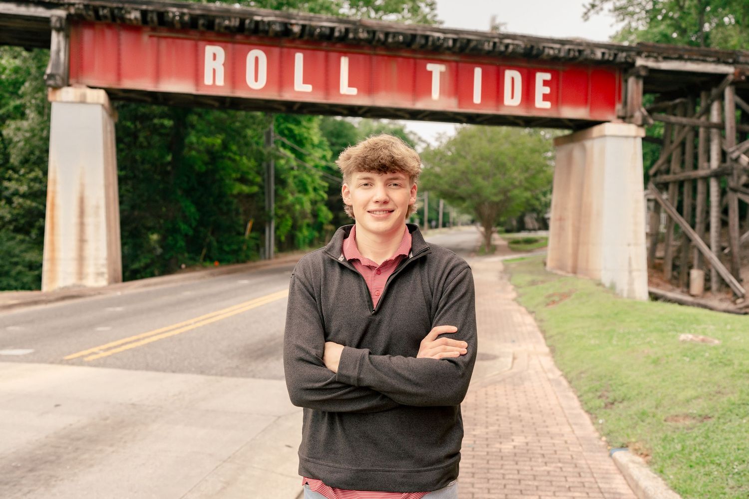 A student smiles while standing beneath the red Roll Tide bridge on campus.