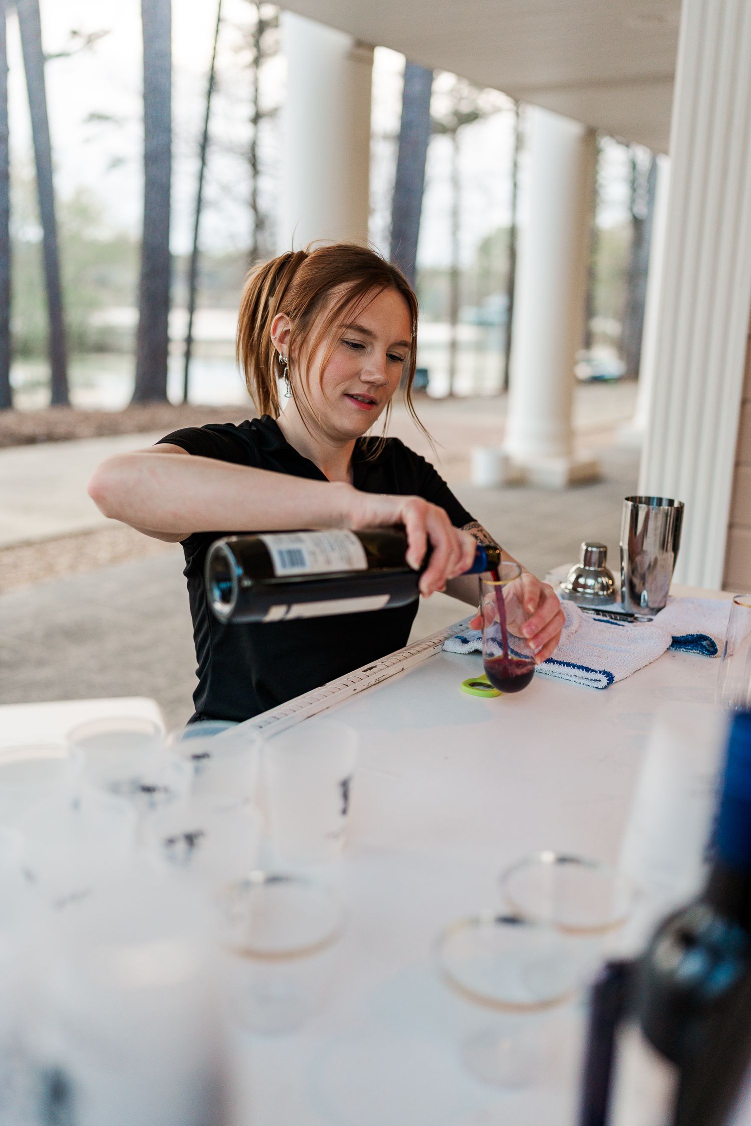 Bartender pouring wine at an outdoor event bar station.