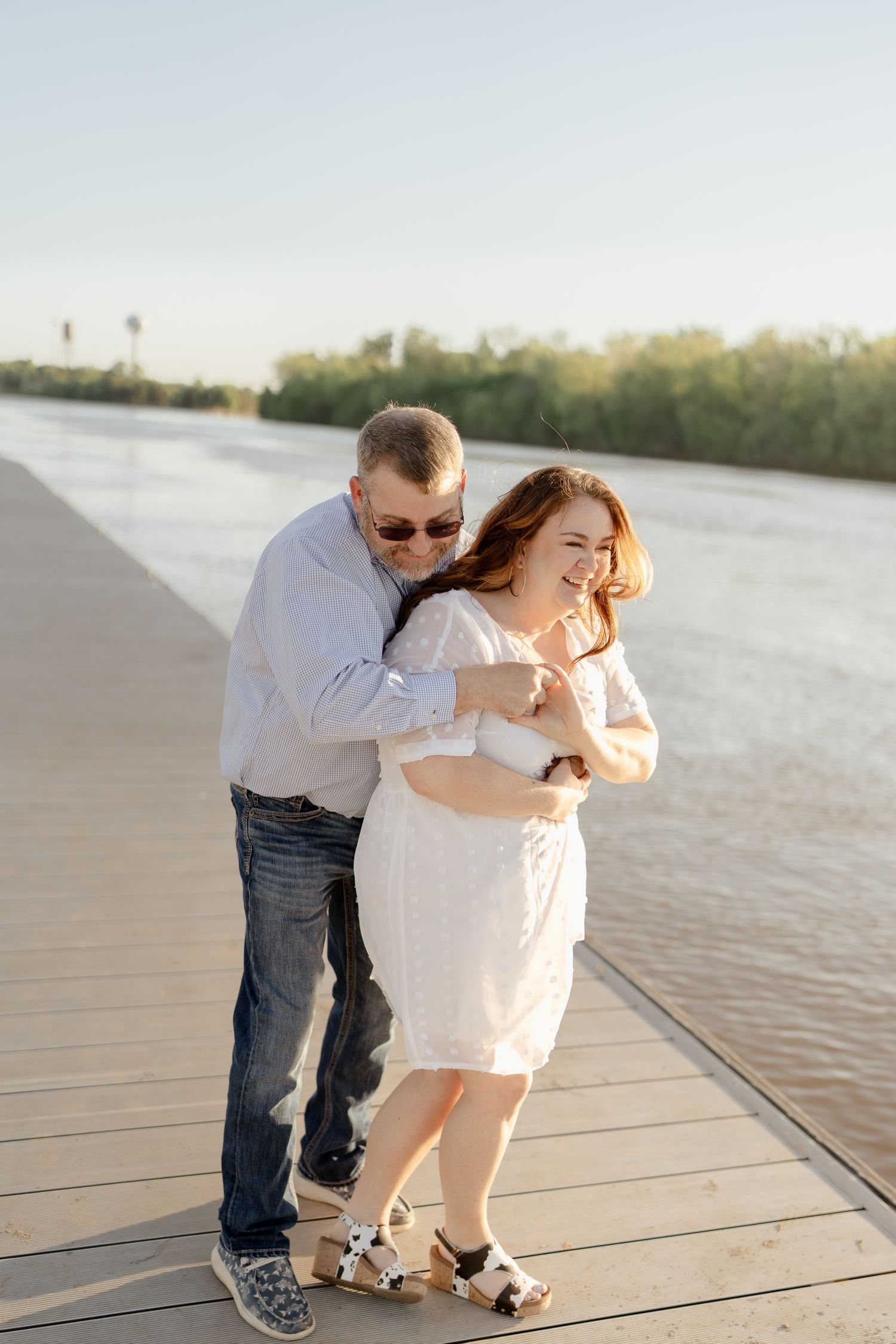 A couple enjoys a tender moment together on a sunny pier by the water.