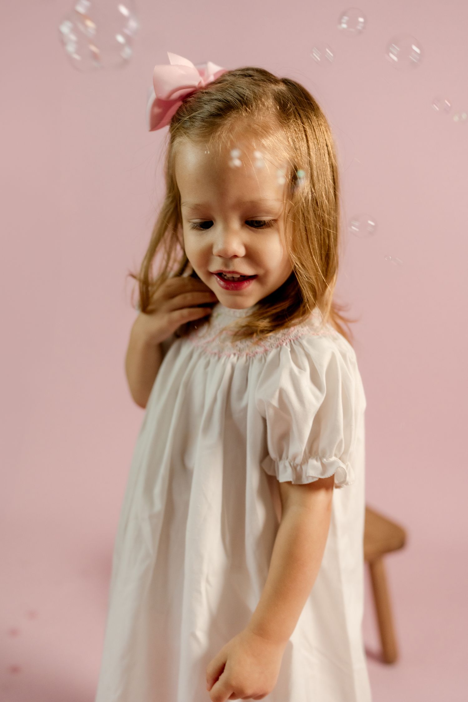 A whimsical portrait with soap bubbles floating around a child in a white dress.