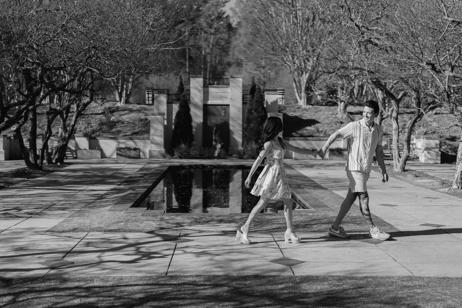 Black and white photo of two people walking past a reflective sculpture in a sunny outdoor park.