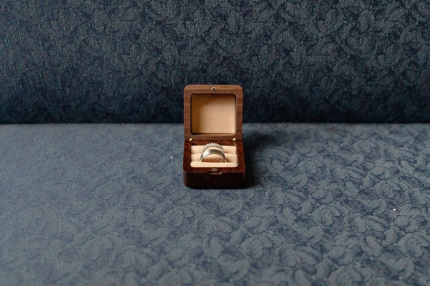 A wedding ring box sits open on a dark textured surface, displaying an elegant engagement ring.