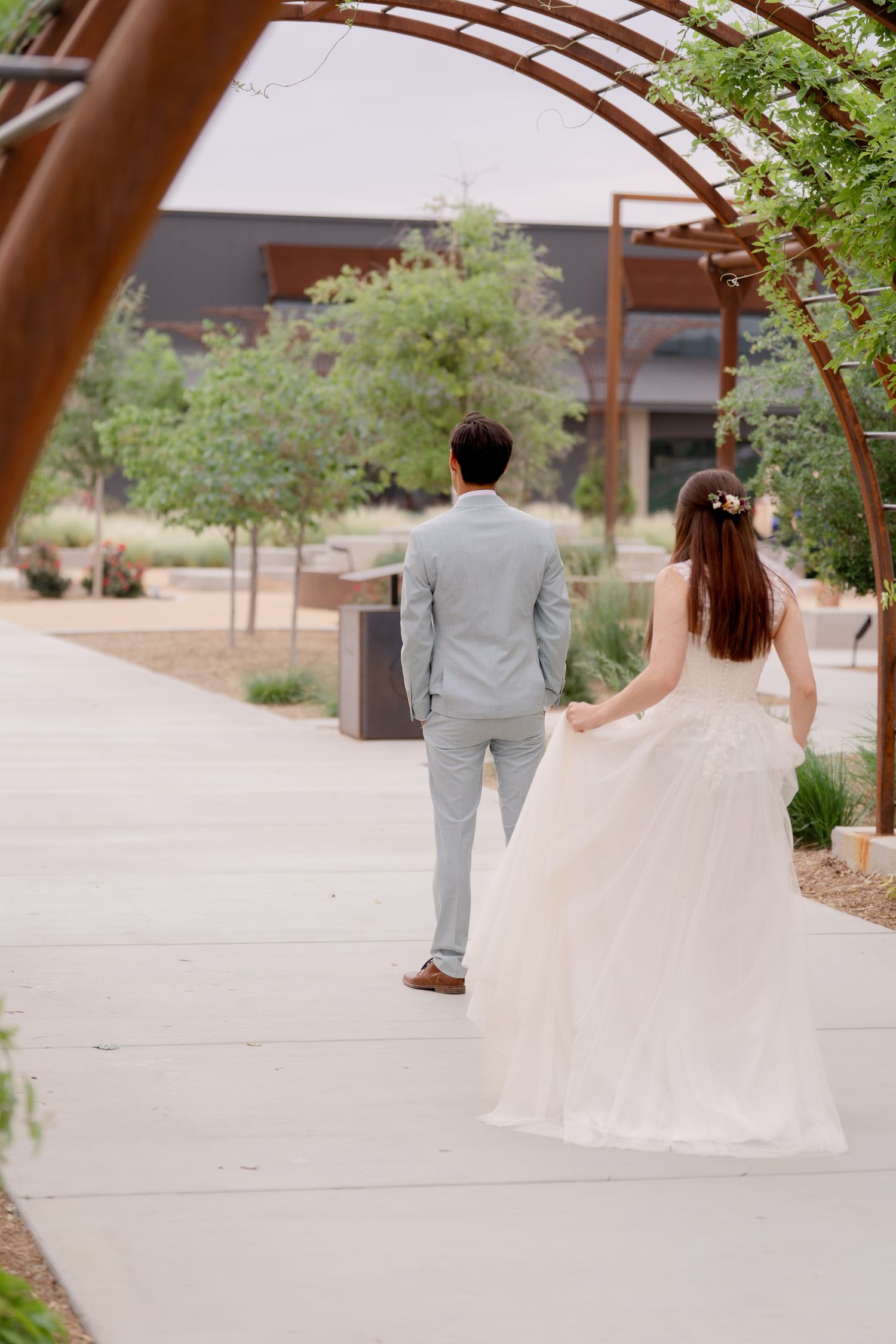 A couple in wedding attire walks hand in hand along a desert garden pathway at an outdoor venue.