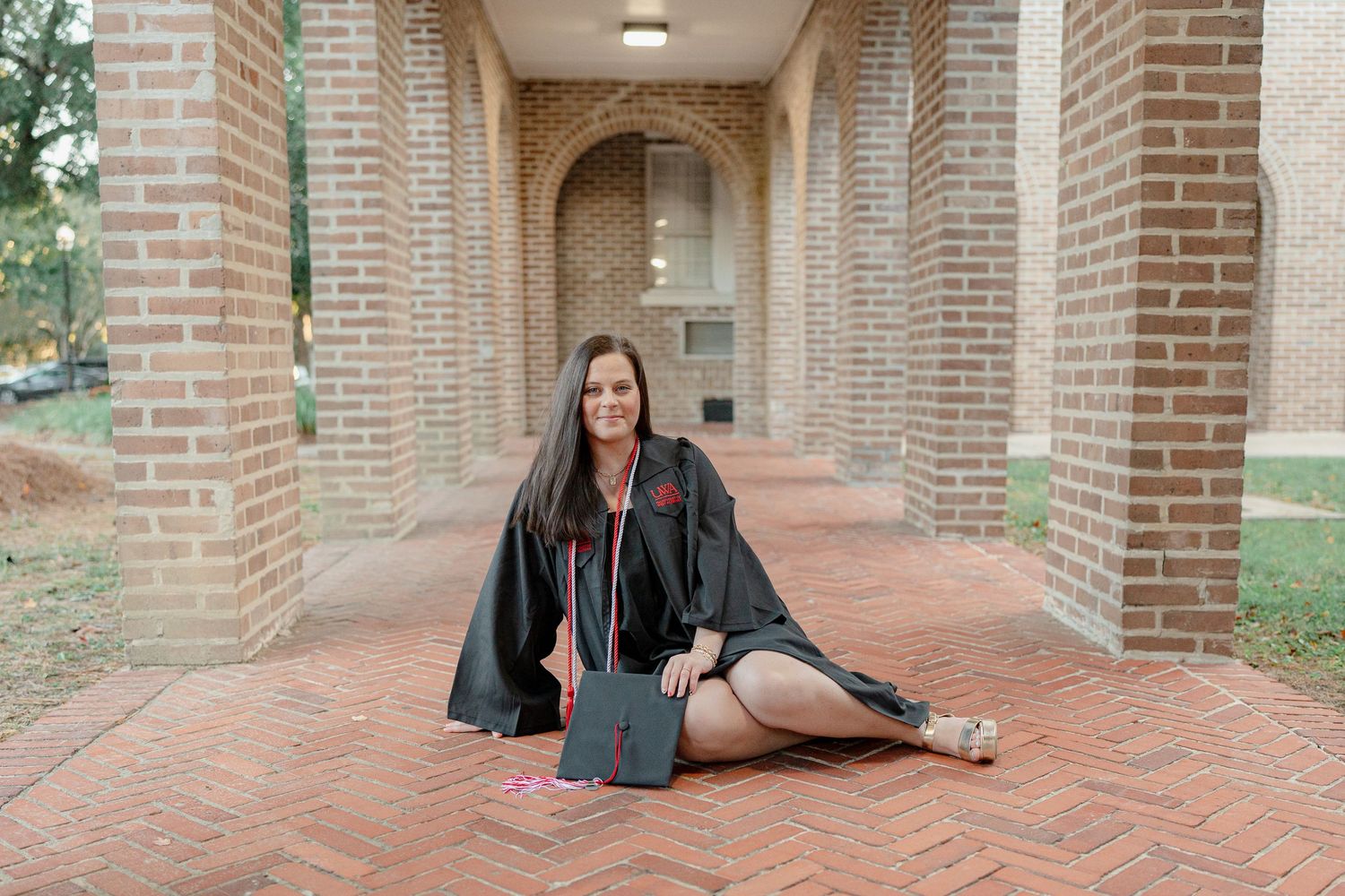 Graduate poses in an arched brick walkway with cap and gown on brick pavement.