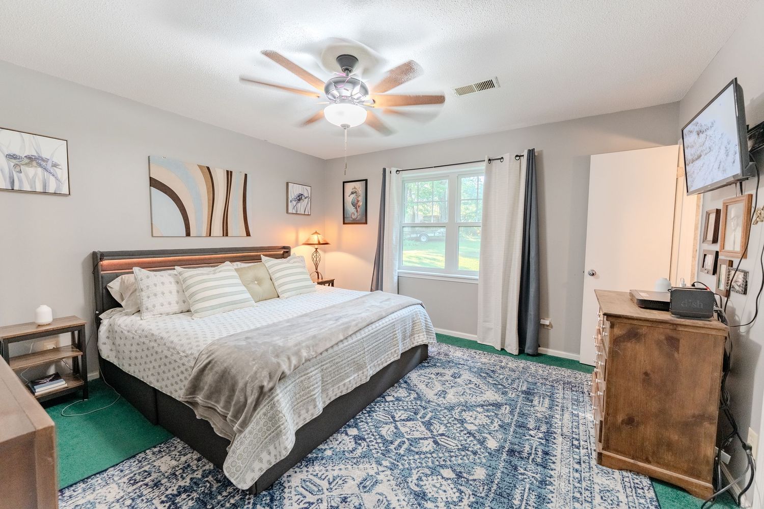 Interior bedroom with ceiling fan, large windows, gray bedding, and rustic wooden furniture.