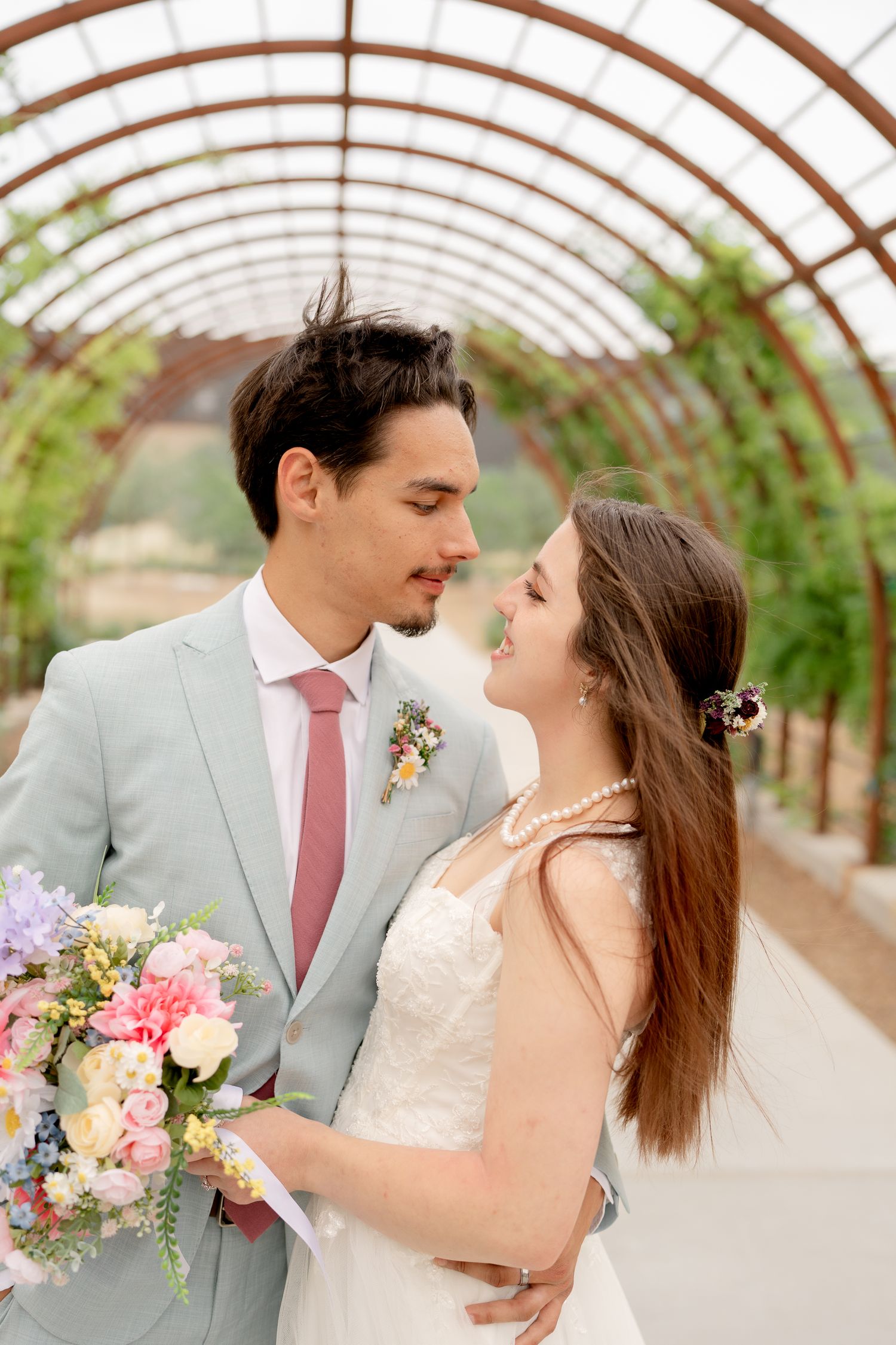 Wedding portraits in a greenhouse featuring soft natural light and pastel floral bouquet.