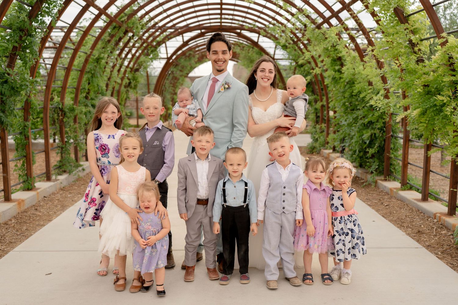 Children and adults gather in a rustic wooden greenhouse walkway for a special occasion.
