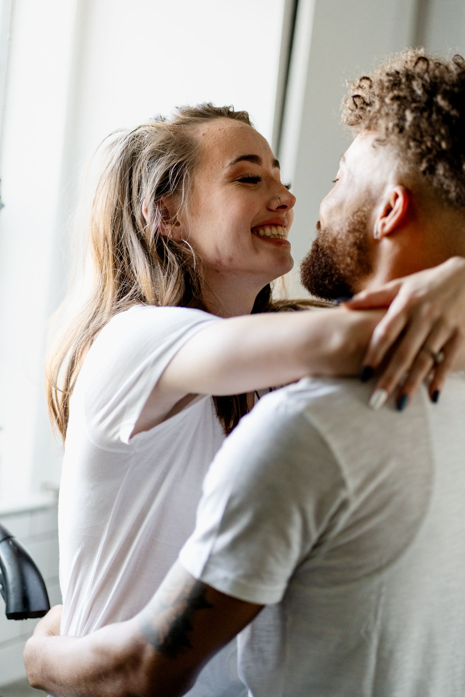 An intimate moment captured between a couple in white shirts against a bright window.