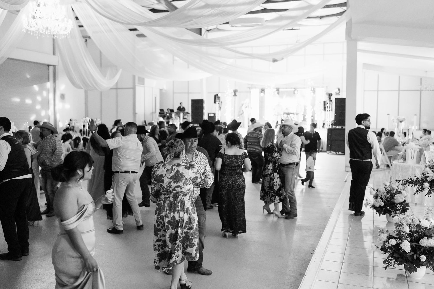 Black and white photo of a wedding reception venue with guests mingling under draped fabric decor.