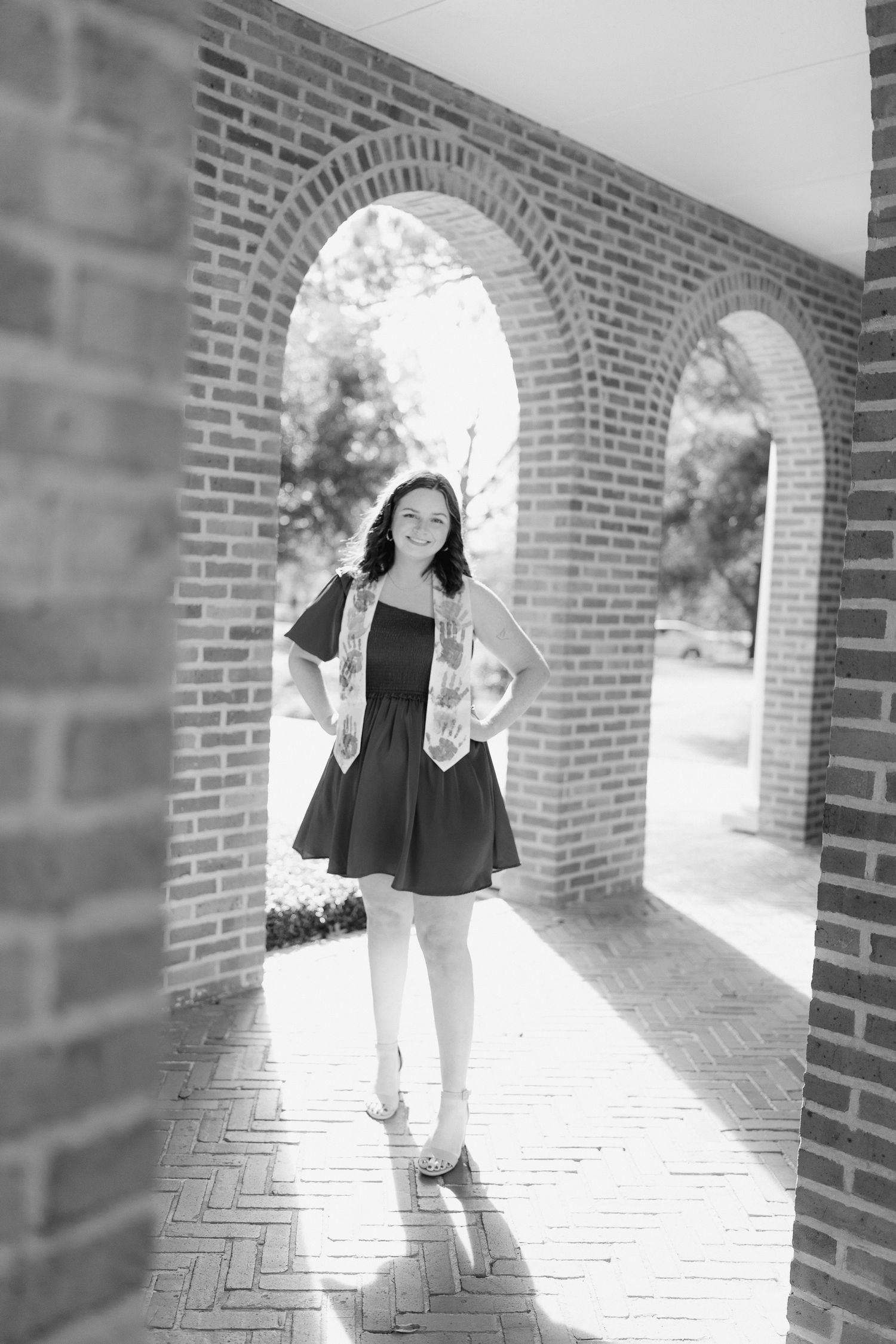 Black and white portrait of someone posing under brick archways with sunlight streaming through the arches.