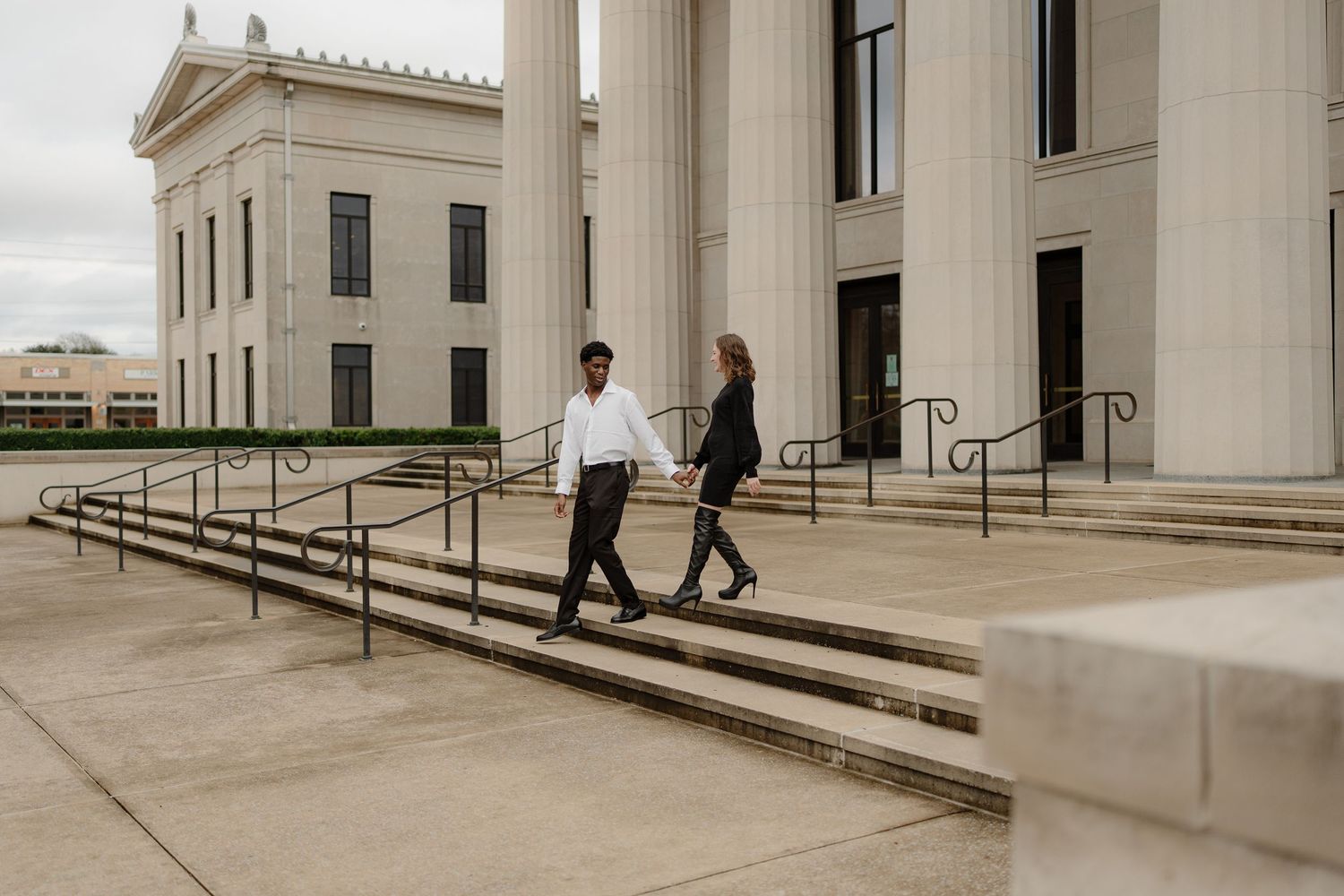 Couple walking hand in hand down steps of a grand neoclassical building with large white columns.