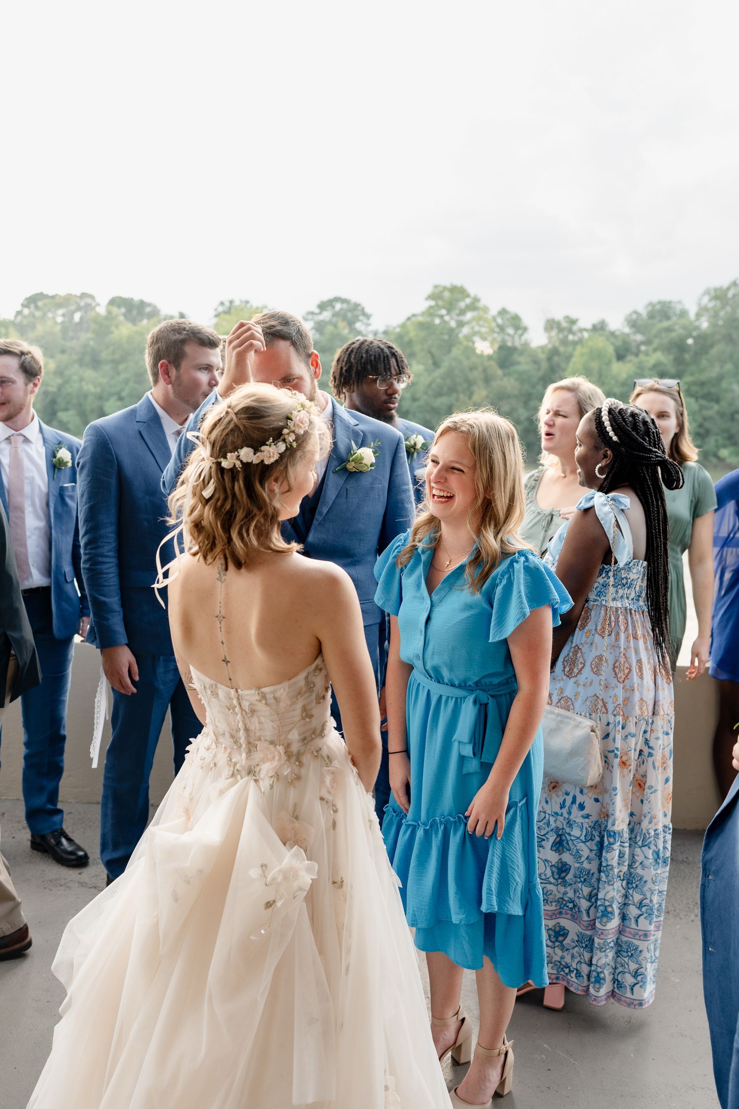 Wedding guests in blue dresses and formal attire gather outdoors for celebration.