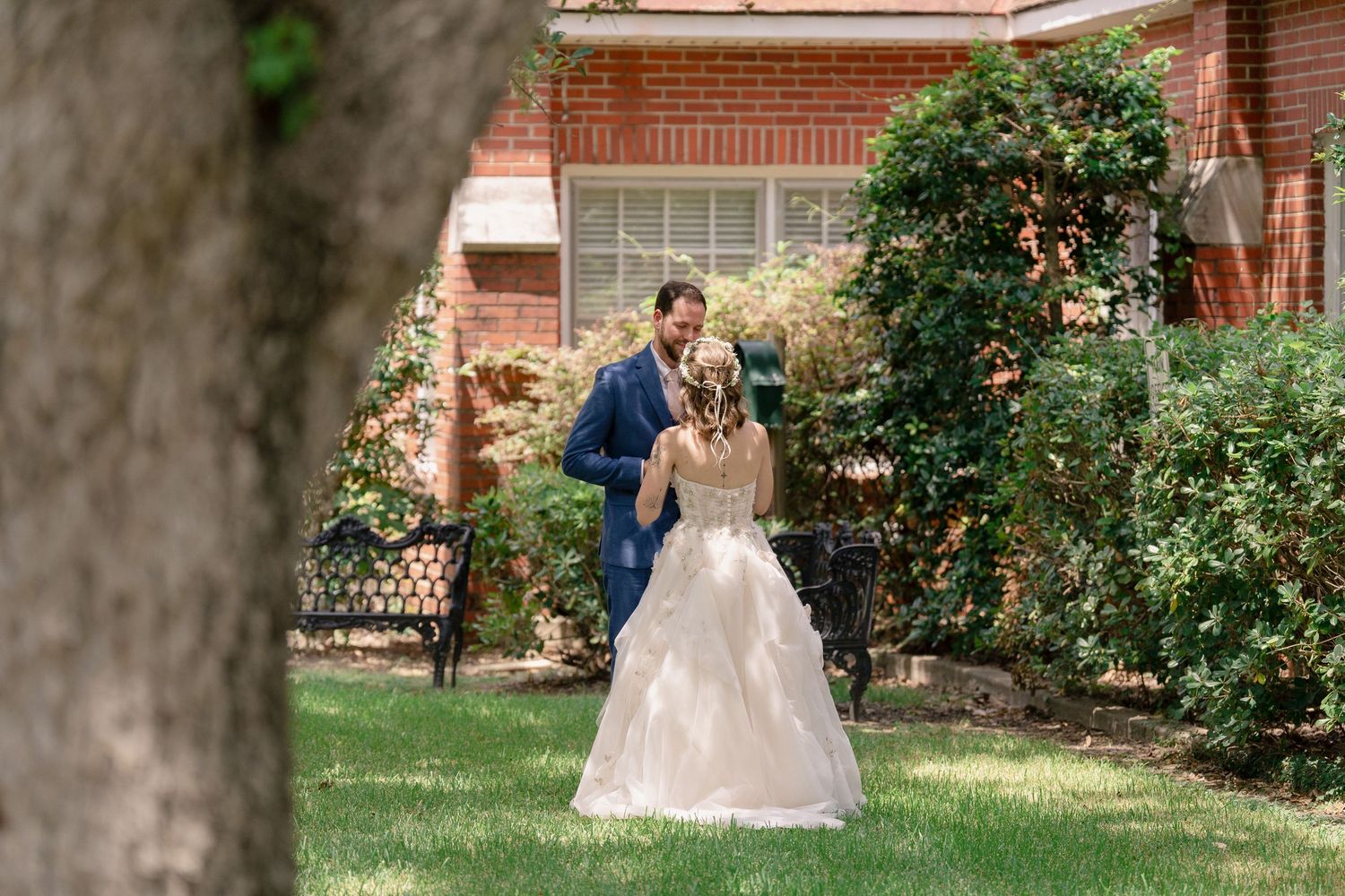 A couple shares a romantic moment in a garden setting with blooming roses and brick architecture in the background.