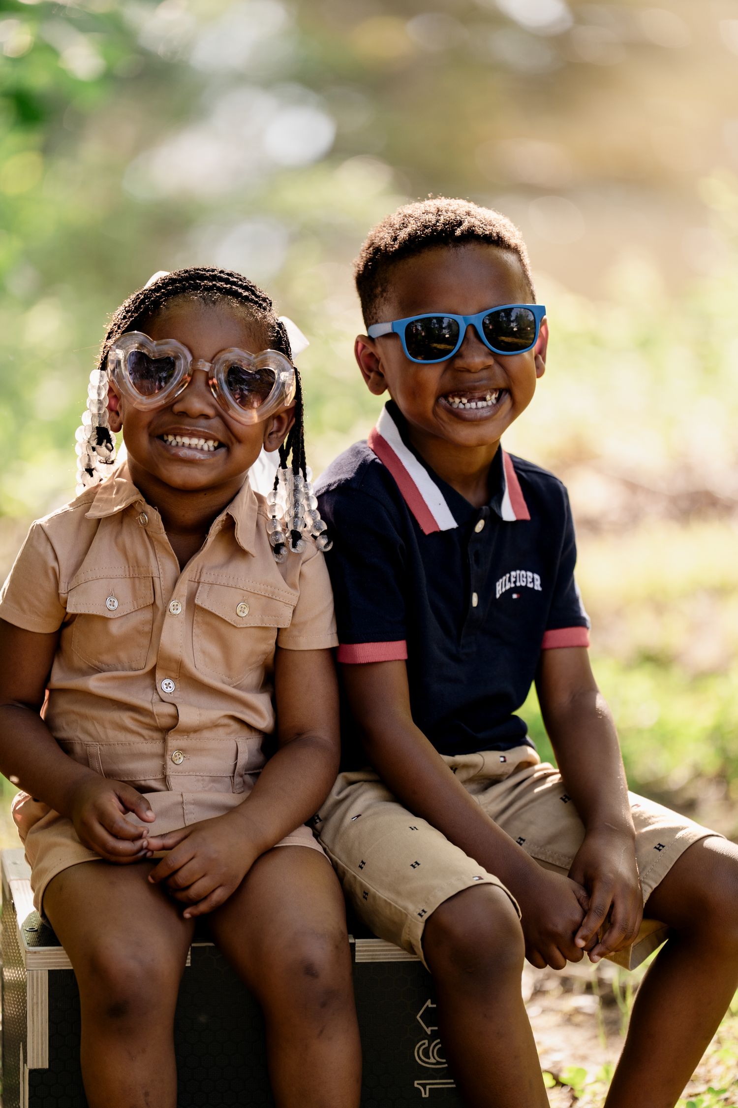 Children wearing sunglasses and casual clothing smile together outdoors.