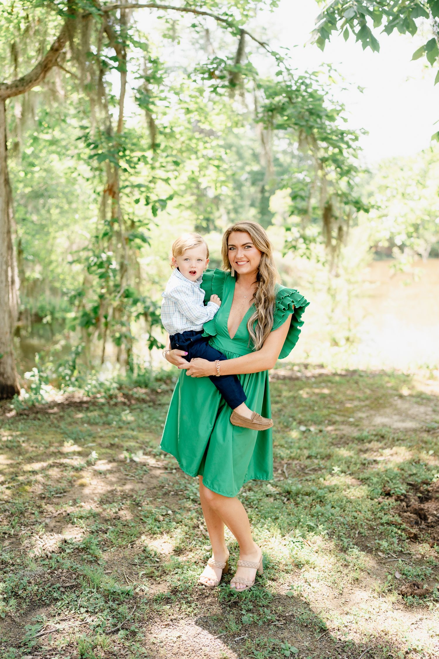 Mother and child playing in a sunlit forest wearing coordinated green and white outfits.