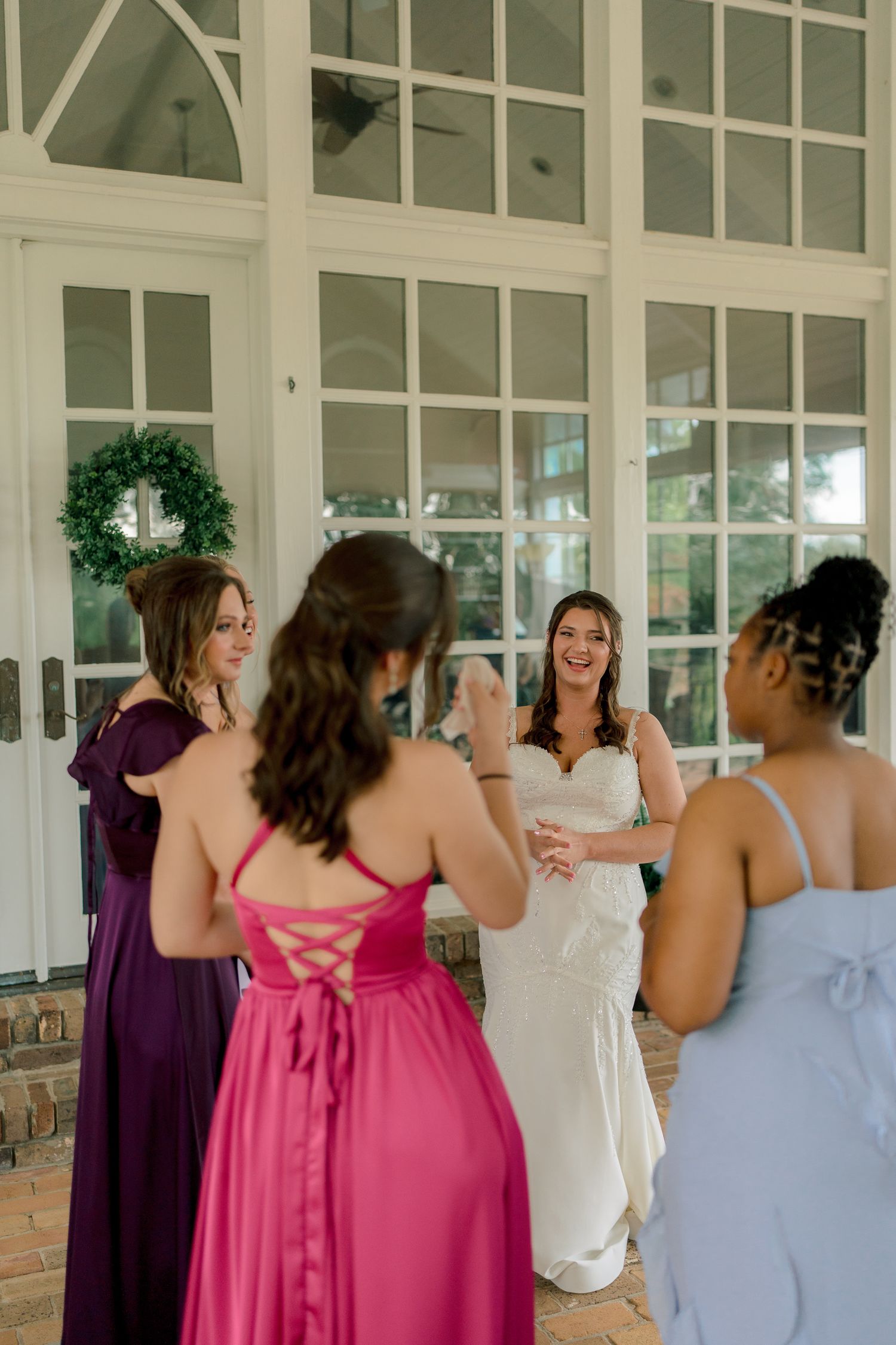 Bride in white gown celebrating with bridesmaids in colorful dresses outside elegant white venue doors.