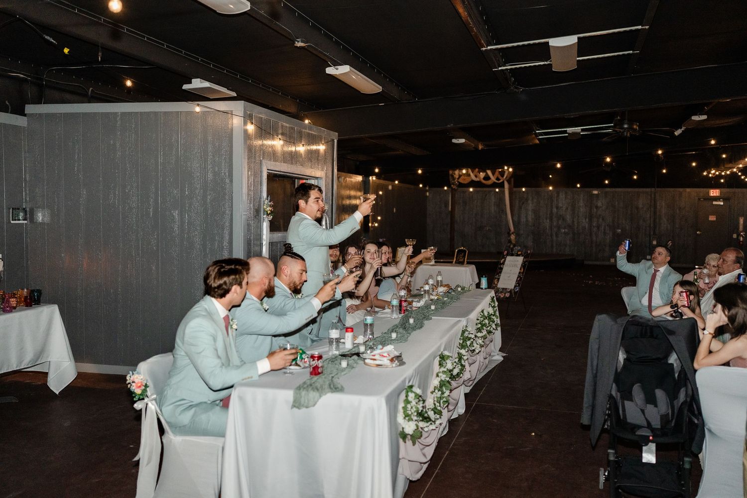 Wedding guests celebrate on the dance floor during a reception with their arms raised in the air.