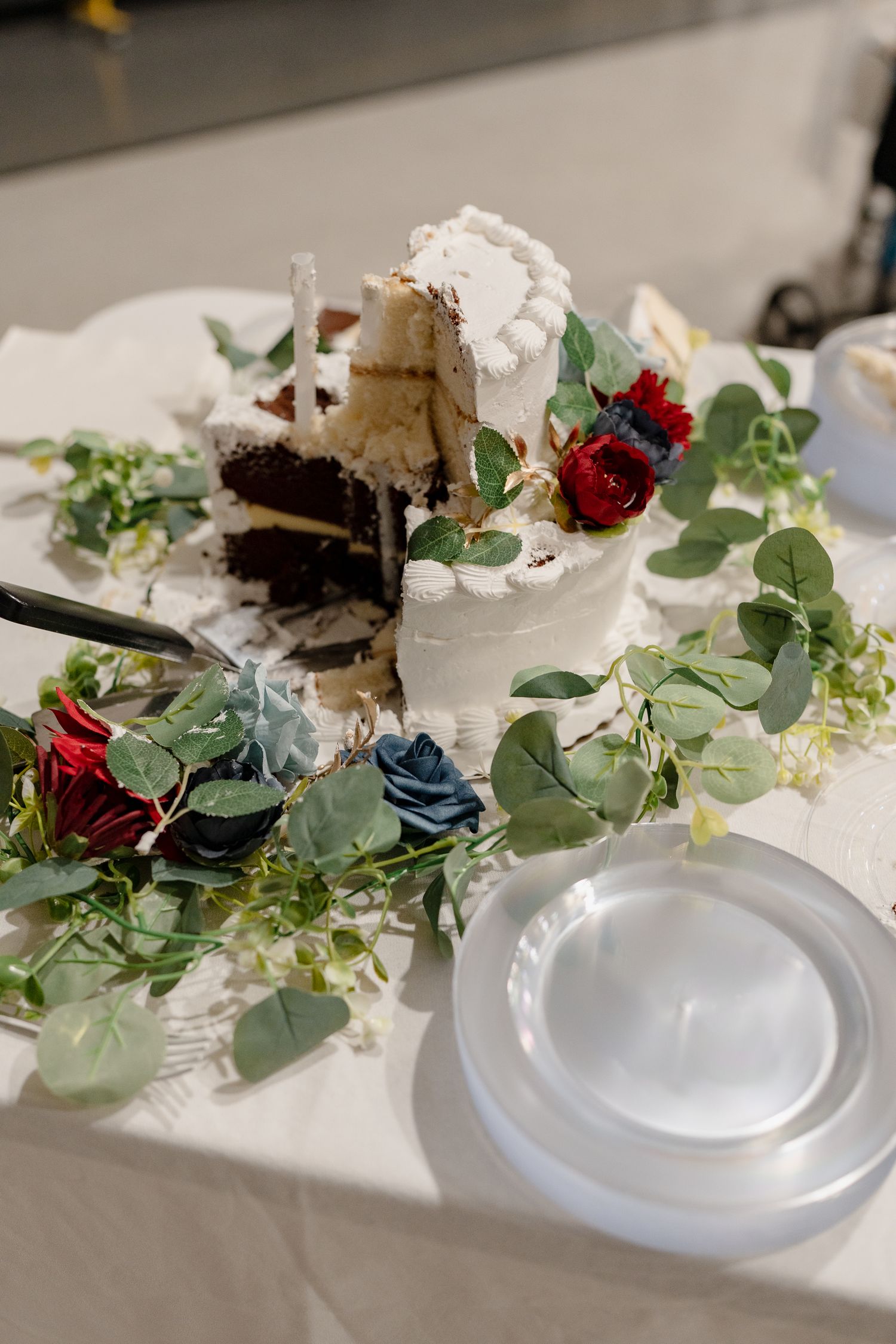 Wedding table decorated with eucalyptus greenery, red roses, and white place settings.