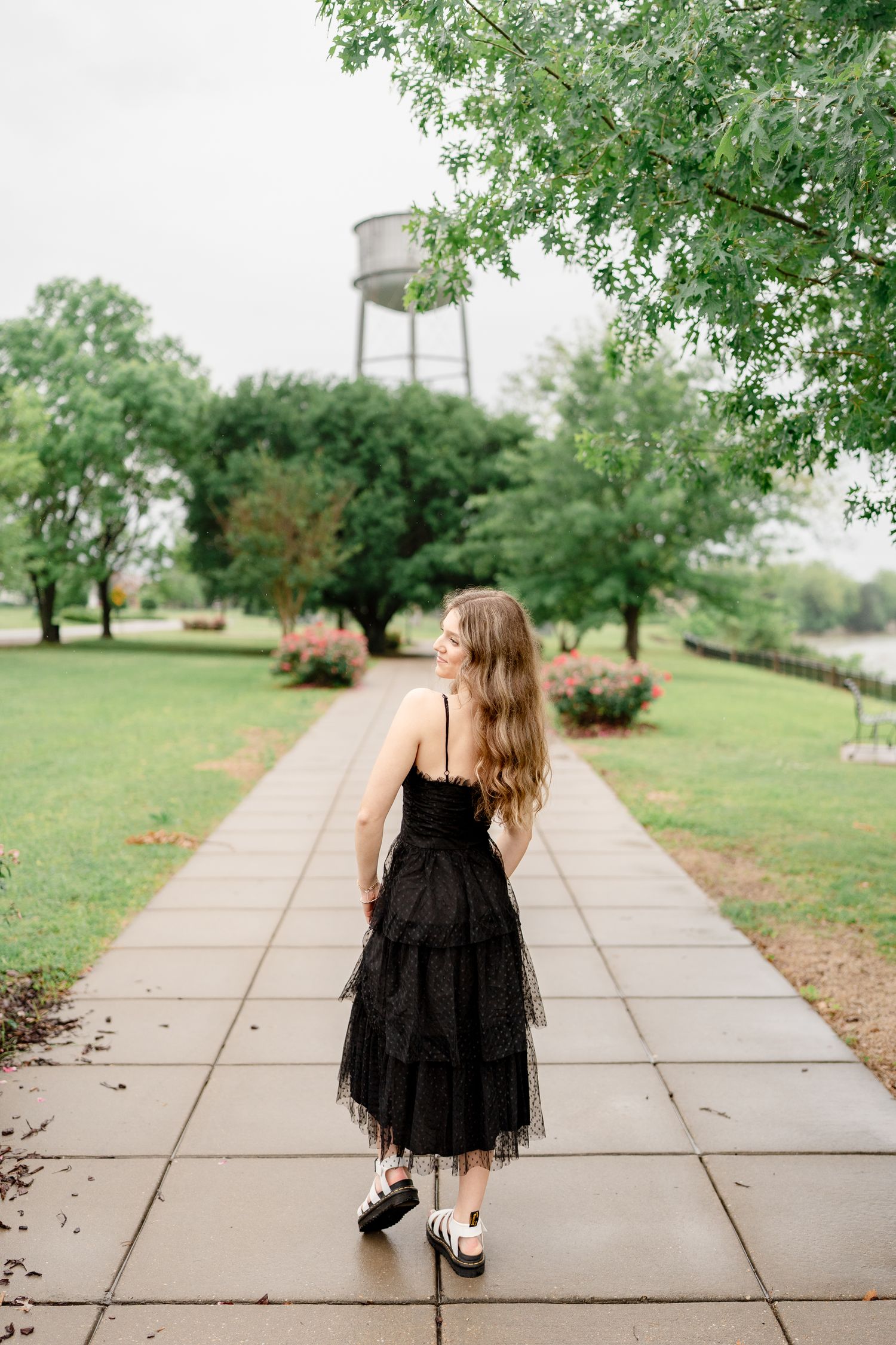 Black dress fashion photography on tree-lined concrete walkway.