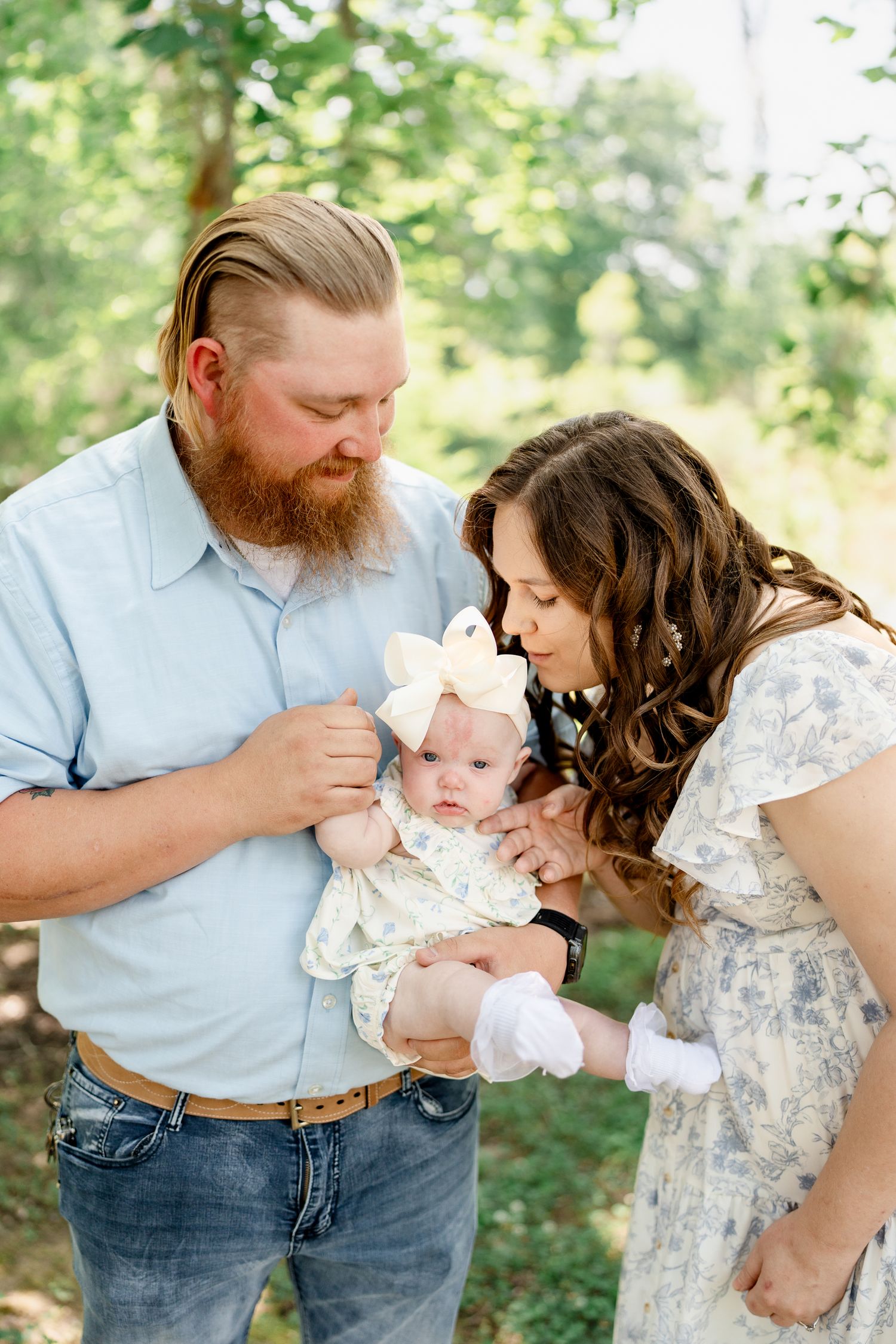Parents sharing sweet moments with infant baby in sunny forest setting.