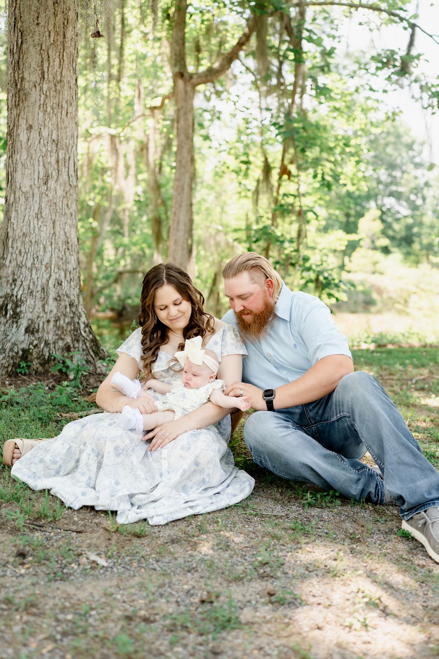 Family relaxing together on ground during outdoor photo session in wooded area.