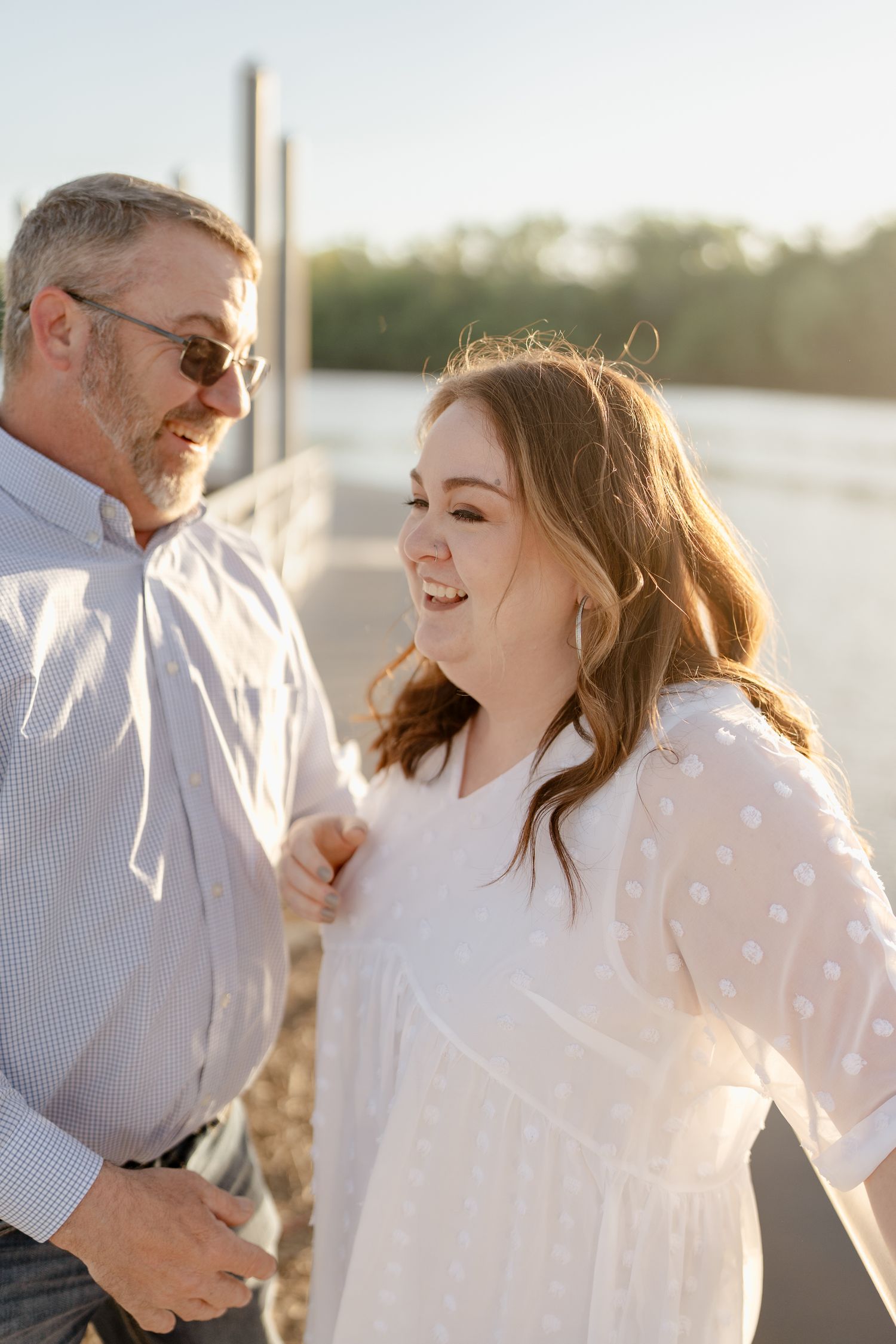 Two people share genuine laughter during a sunny waterfront photo session.