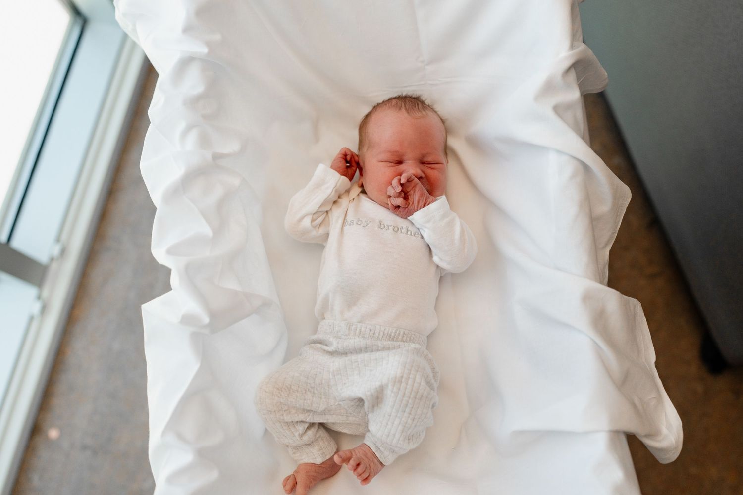 Newborn in white clothing sleeping peacefully on crisp white bedding.