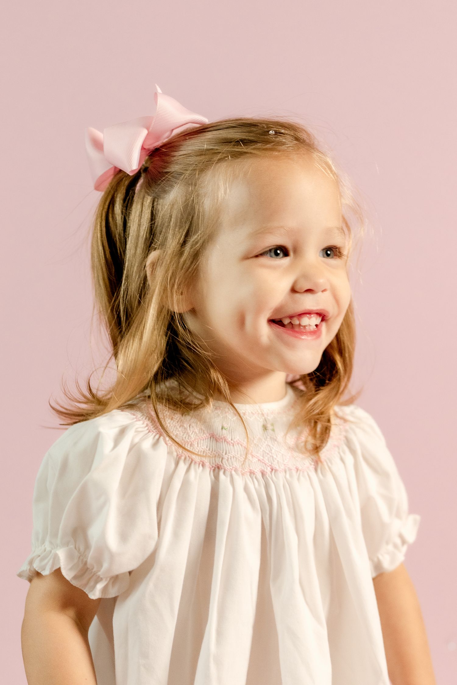 A sweet portrait showing genuine laughter against a pink studio background.