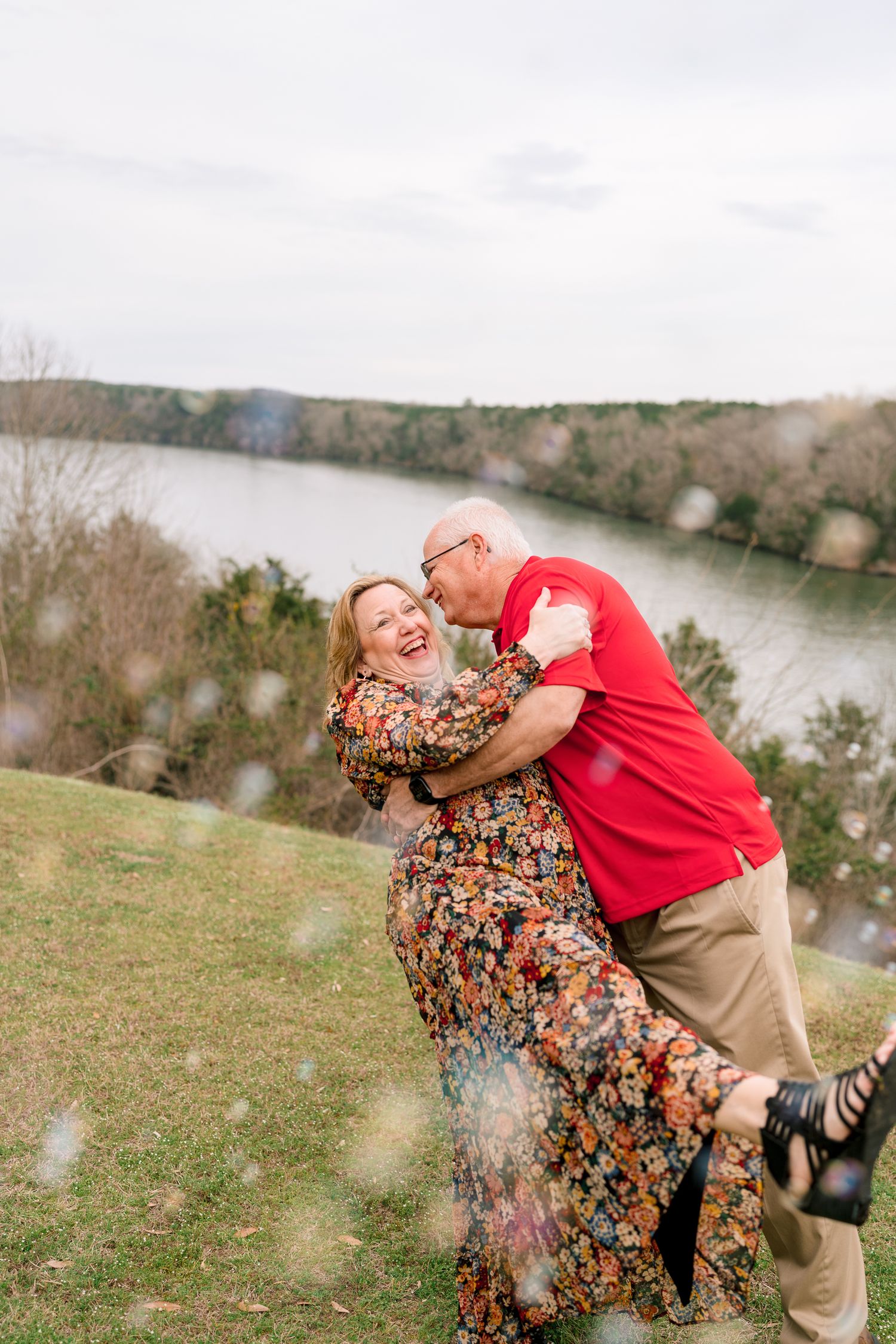 Joyful older couple embracing and laughing outdoors near a scenic river overlook.