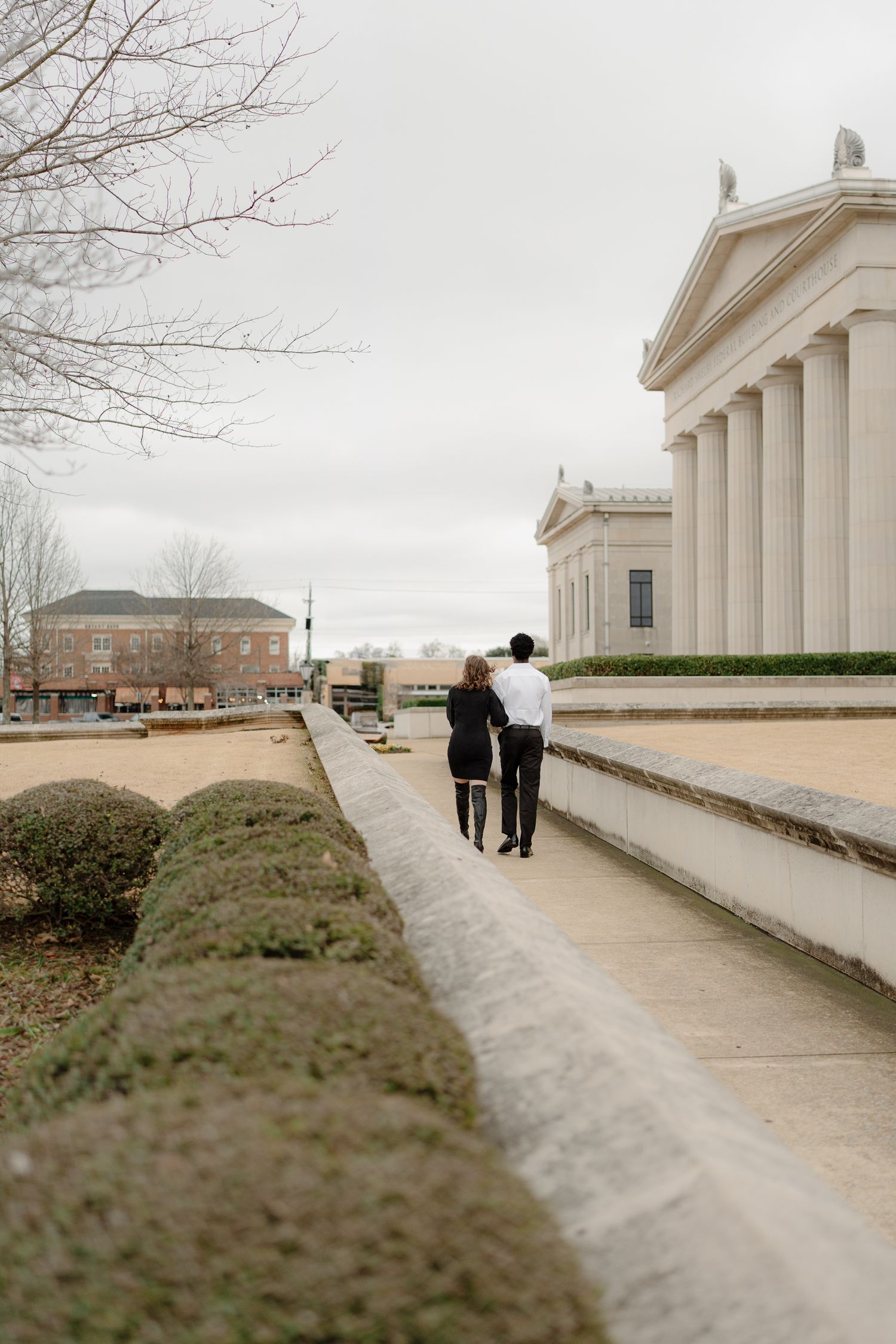 Couple walking together along a neoclassical building pathway on an overcast day.