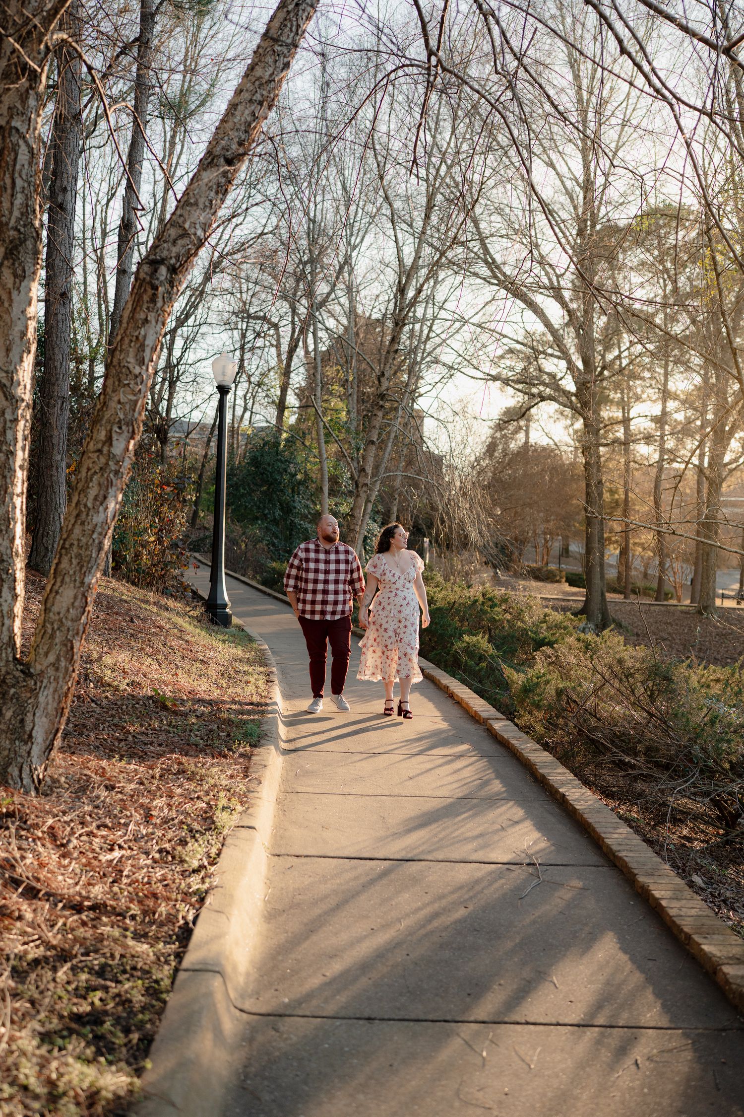 Couple walking together on winding park path during golden hour with bare winter trees.