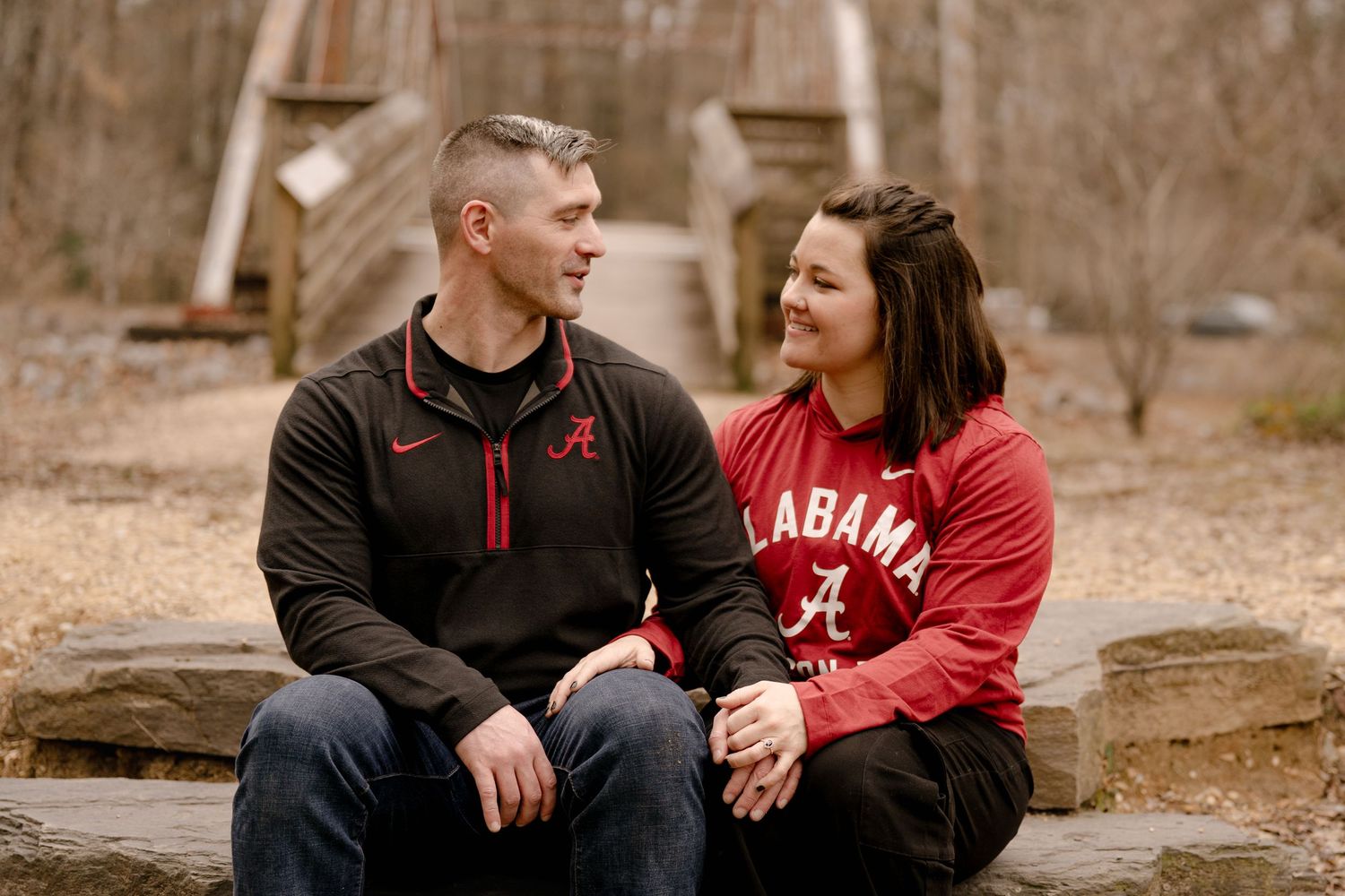 A couple in matching red and black outfits sits together outdoors during a romantic winter photo session.