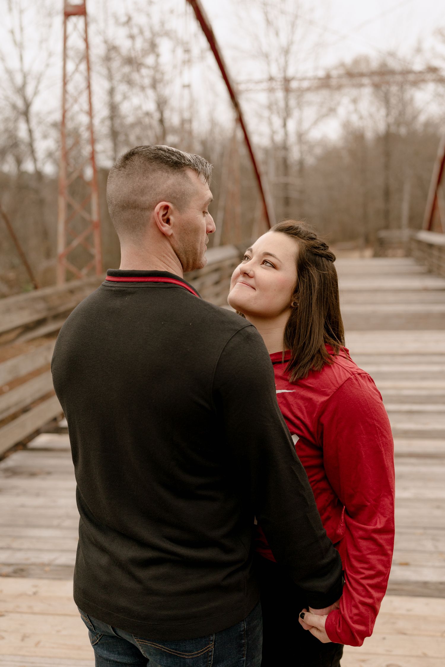 A couple in red and black outerwear share a romantic moment together on a winter path.