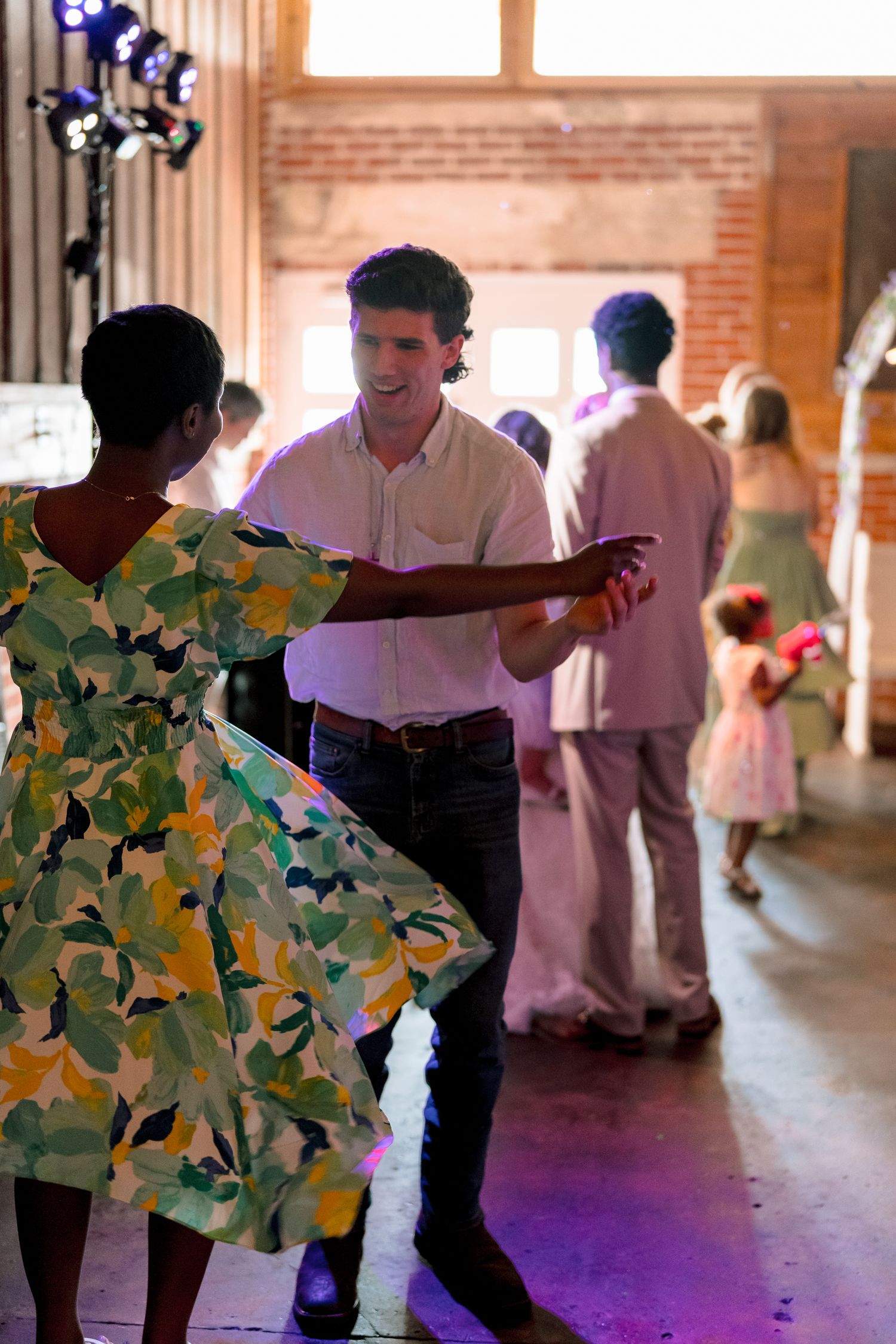 Guests dancing joyfully at a wedding reception inside a rustic brick barn venue.