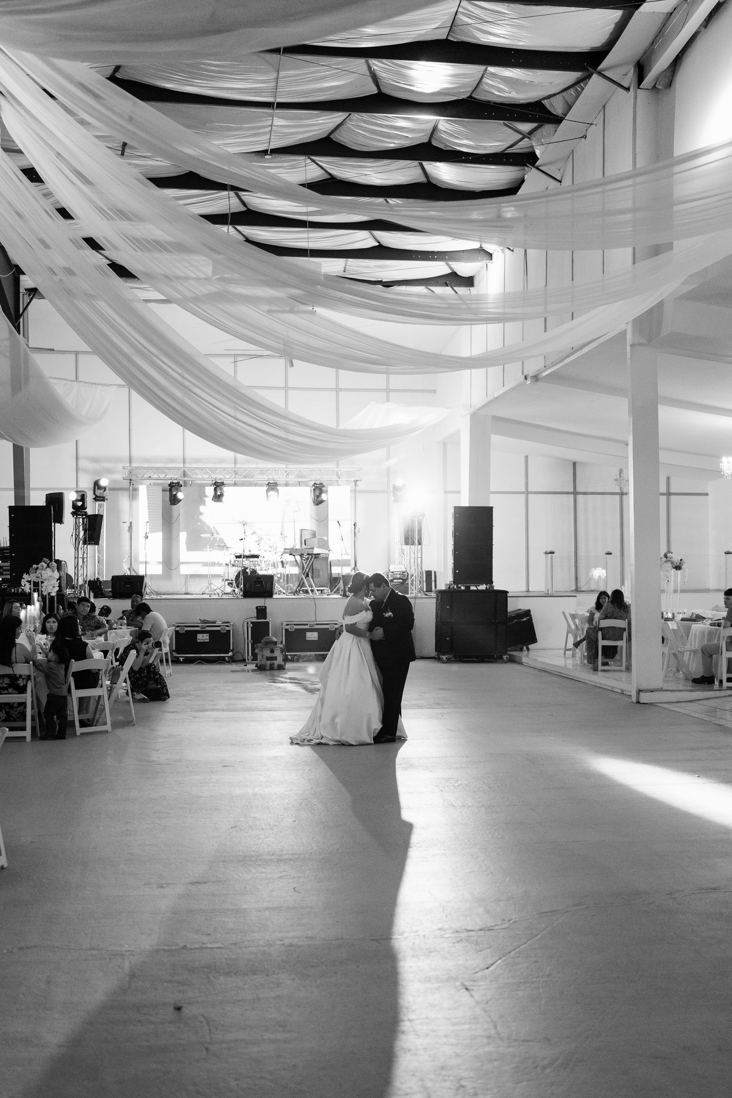 A large indoor venue decorated with white fabric draping from the ceiling and white folding chairs.