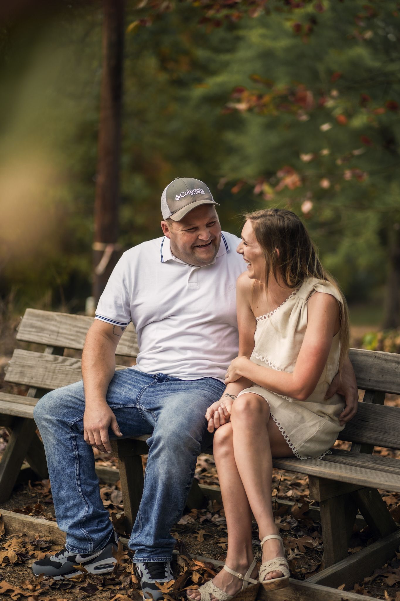 A couple shares a tender moment while sitting on a wooden bench surrounded by fall foliage.