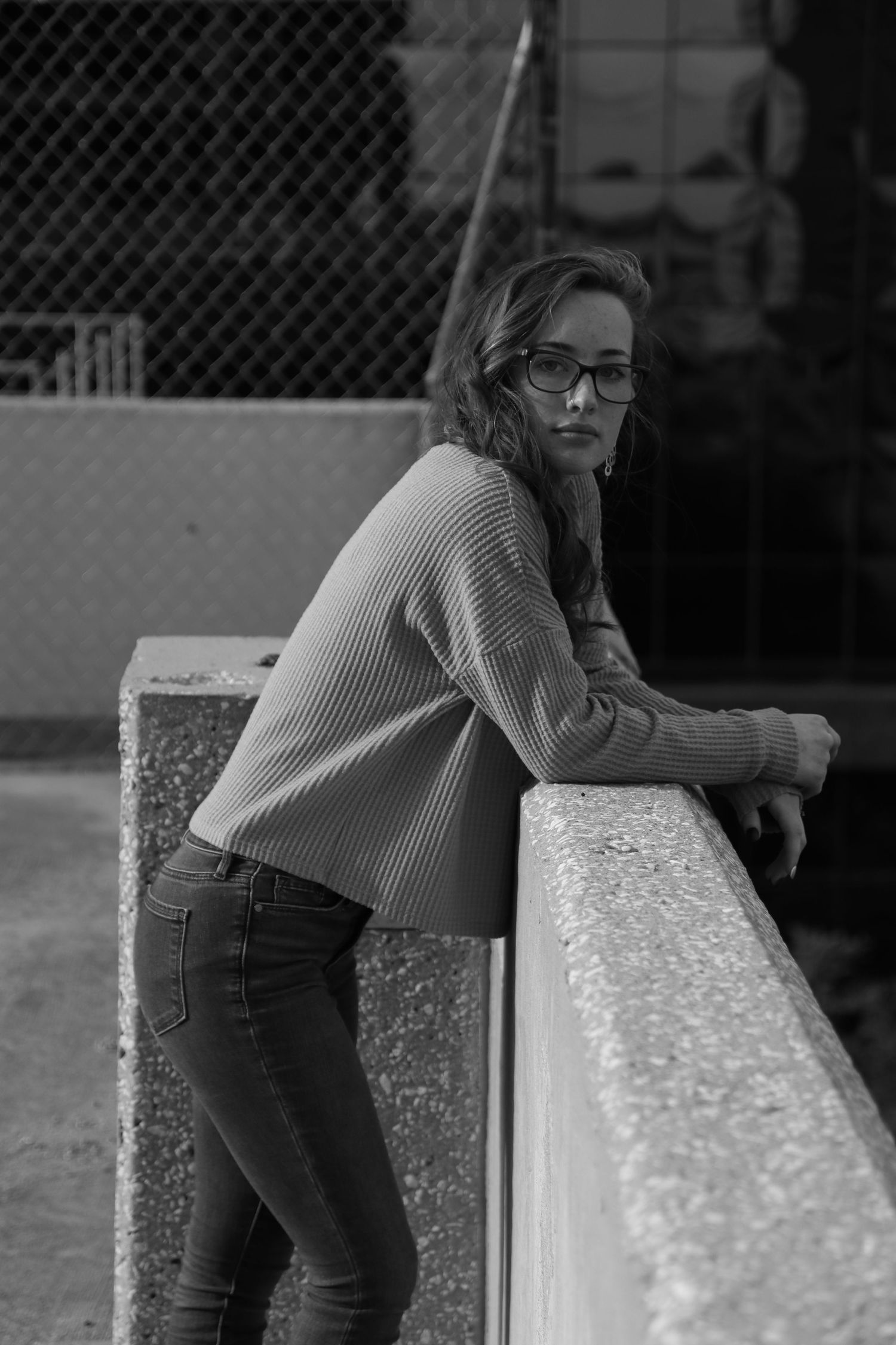 Black and white portrait of woman leaning on concrete ledge wearing sweater and jeans.