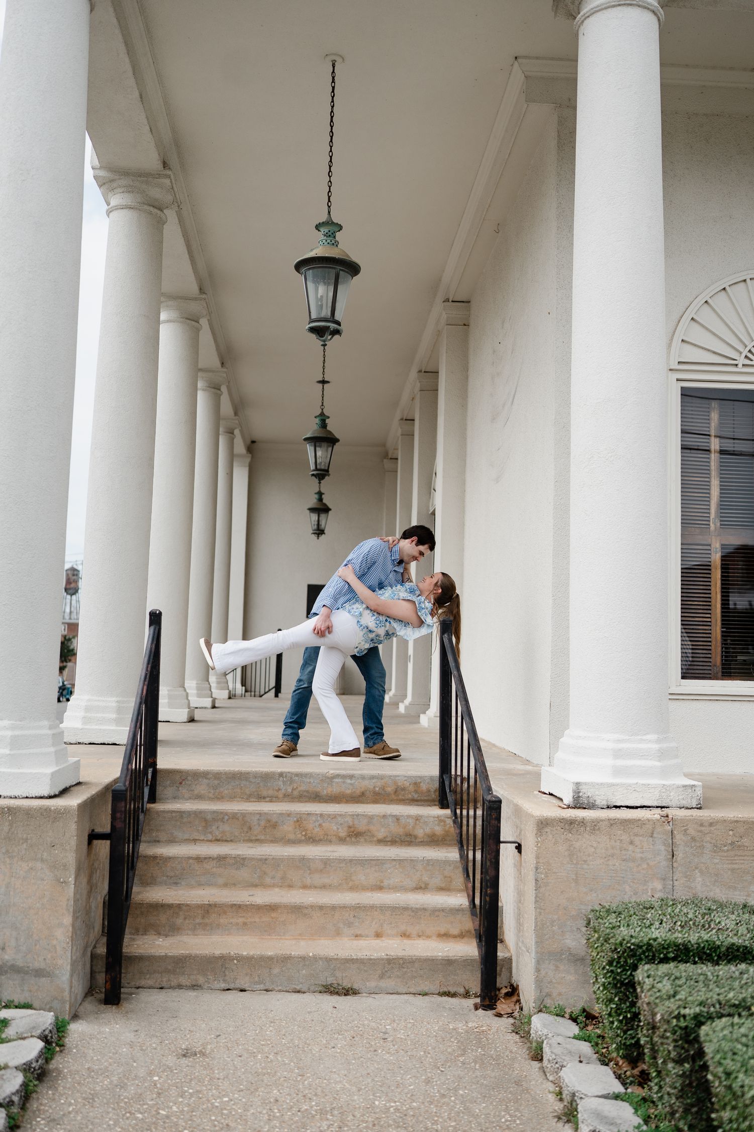 Romantic dip pose between white columns on architectural portico steps.
