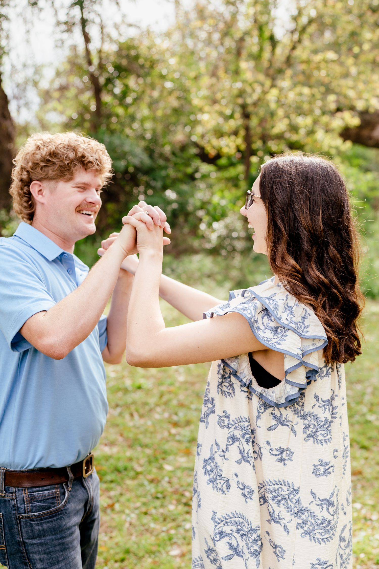 A couple holds hands and laughs together in a sunny outdoor setting.