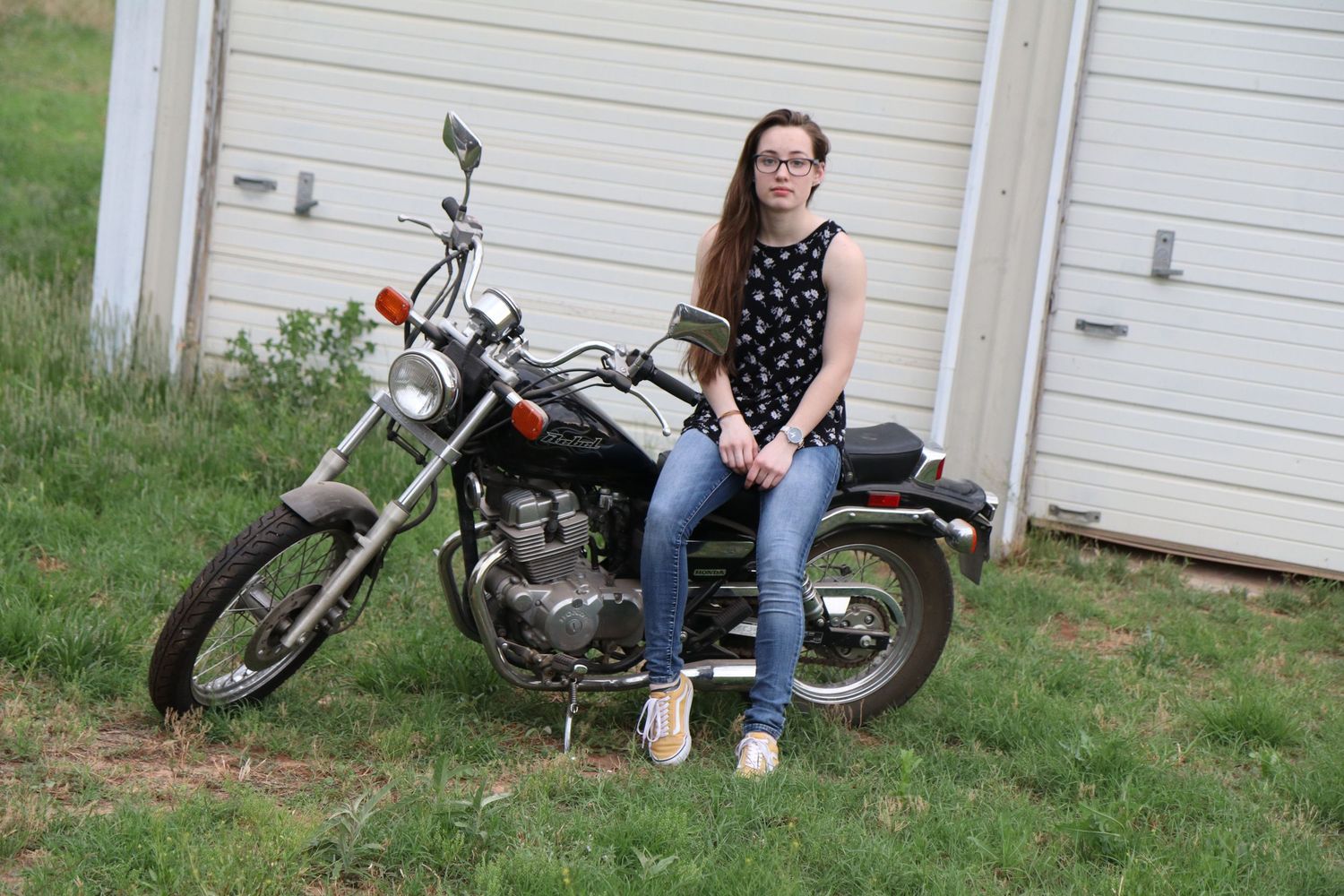 A motorcycle enthusiast poses with a classic bike against white garage doors.