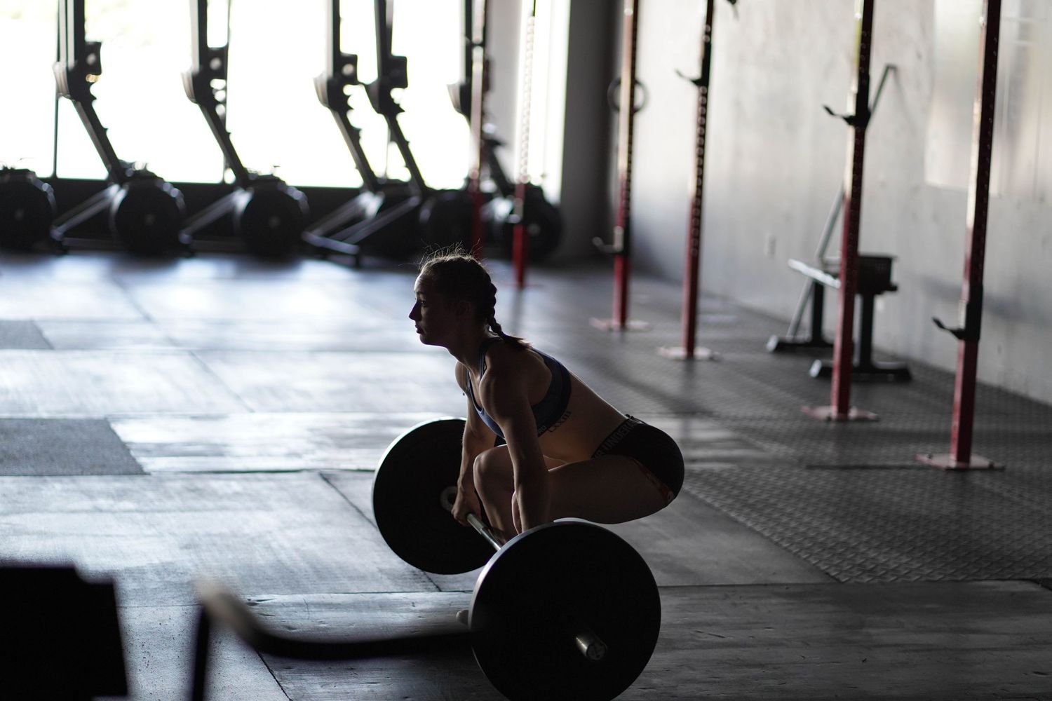 Silhouette of an athlete performing a clean and jerk with a barbell in a gym setting.